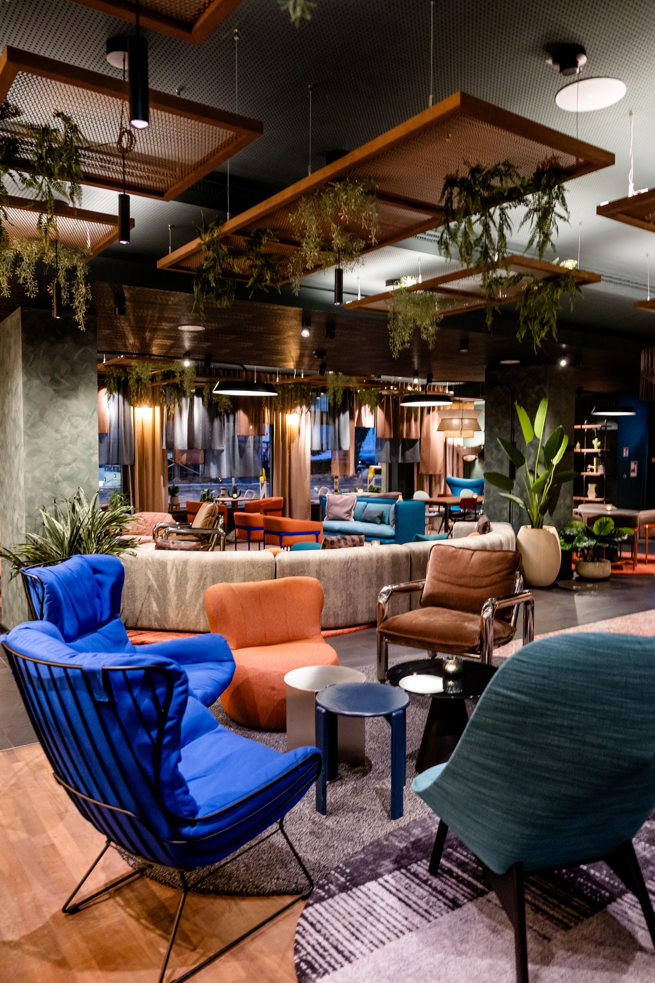 Modern eingerichteter Hotel-Lounge-Bereich mit bequemen Sesseln in kräftigen Farben, dekorativen Pflanzen und stimmungsvoller Beleuchtung, der eine einladende Atmosphäre zum Entspannen und geselligen Zusammensein schafft.