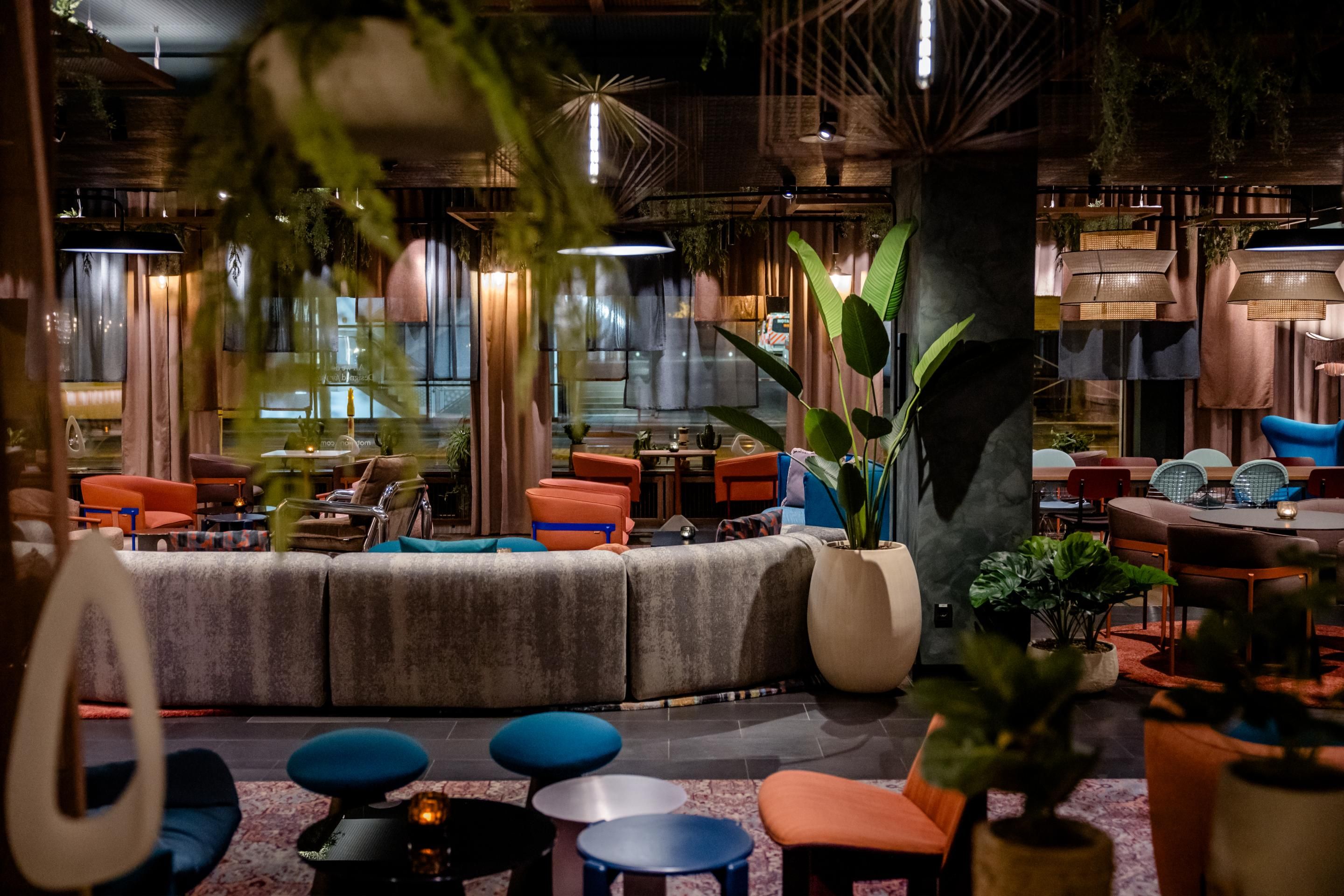 Moderne Hotelbar mit stilvoller Einrichtung, bequemen Sitzmöglichkeiten und warmem Lichtambiente. Große Pflanzen schaffen eine entspannte, einladende Atmosphäre für geselliges Beisammensein.