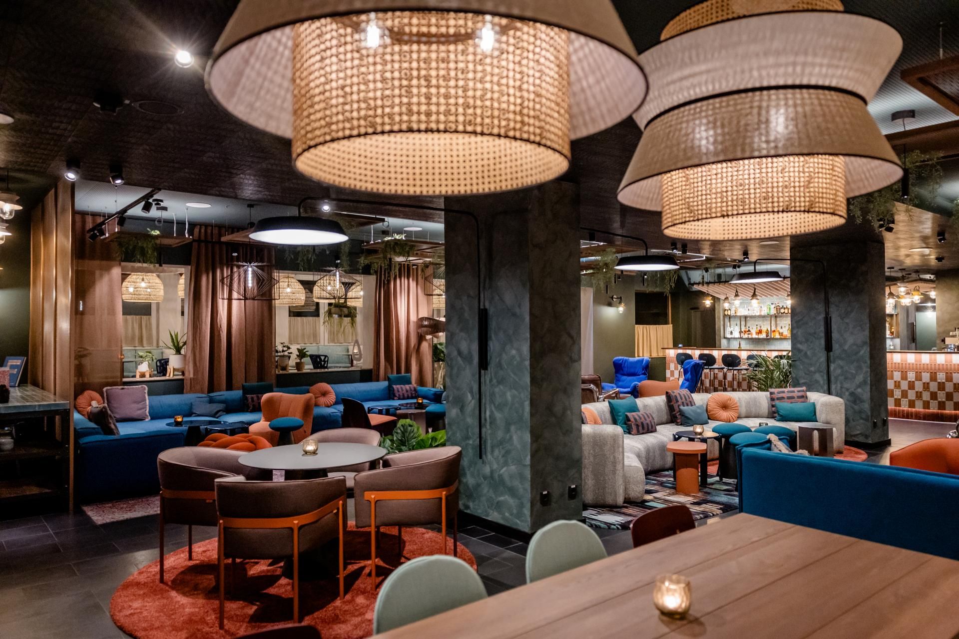 Gemütliche Hotel-Lounge mit stilvollen Sitzbereichen, warmem Licht von großen, texturierten Hängeleuchten und moderner, einladender Atmosphäre für Entspannung und geselliges Beisammensein.