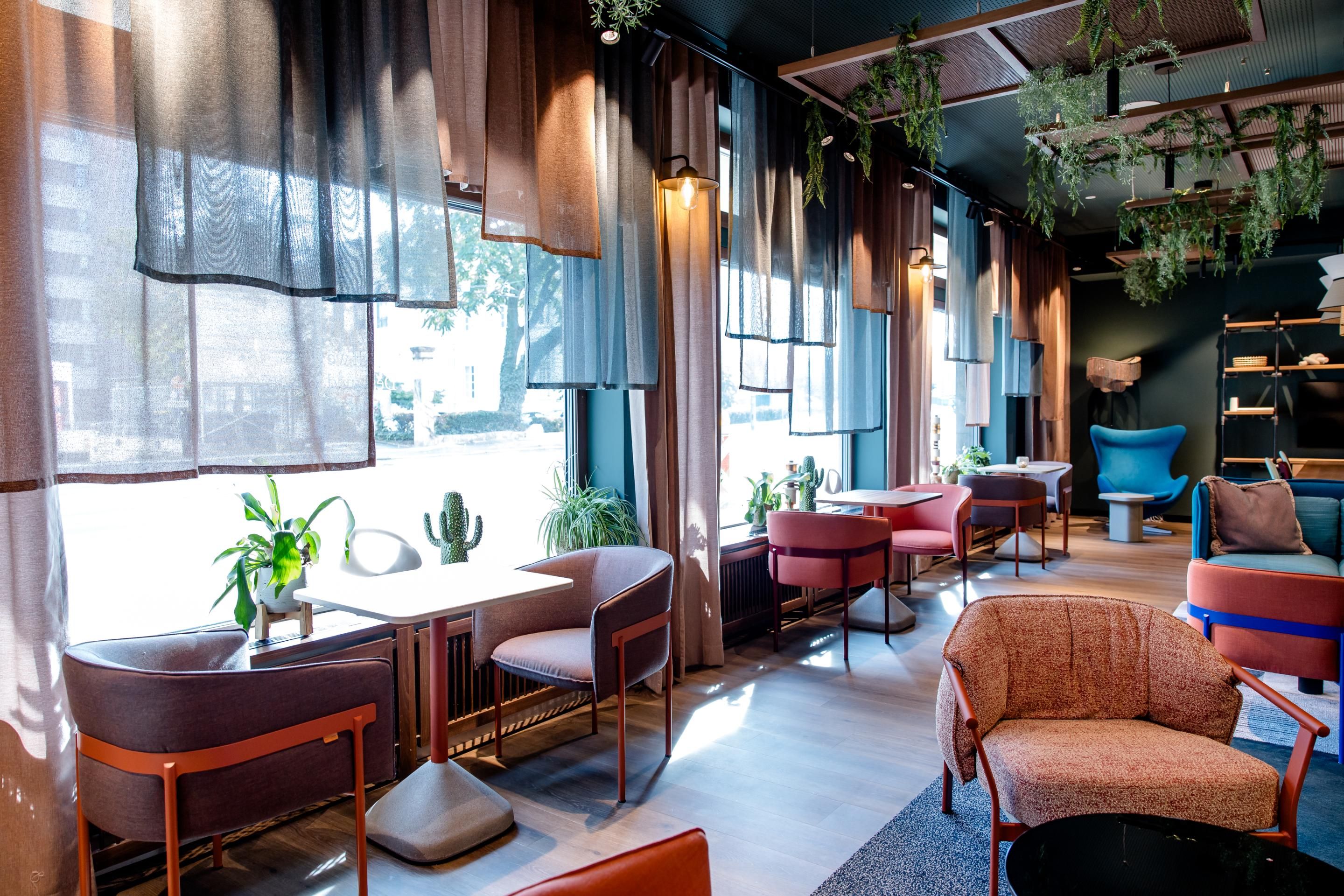 Heller, moderner Lounge-Bereich mit großen Fenstern, gemütlichen Sesseln und Tischen, dekoriert mit Pflanzen und sanfter Beleuchtung, ideal zum Entspannen oder Arbeiten.