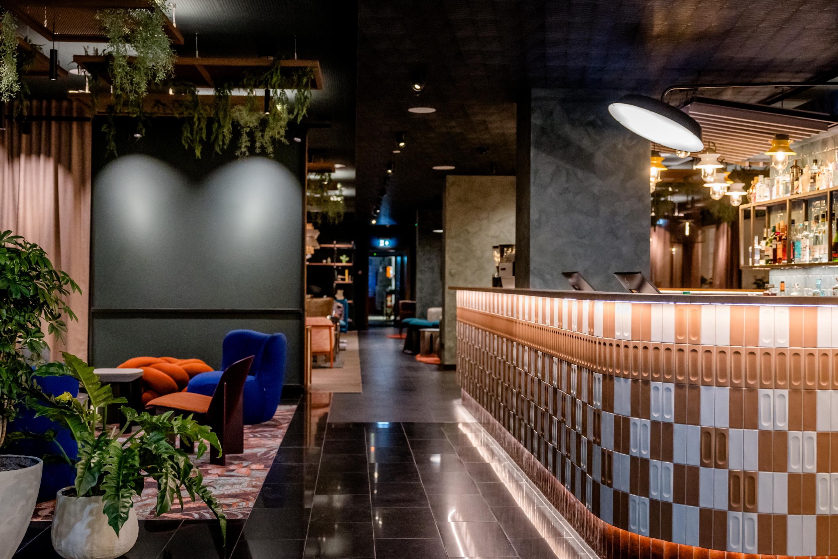 Modern gestaltete Hotelbar mit stilvoller Beleuchtung, bequemen Sitzgelegenheiten und grünen Pflanzen, die eine einladende und entspannte Atmosphäre schaffen.
