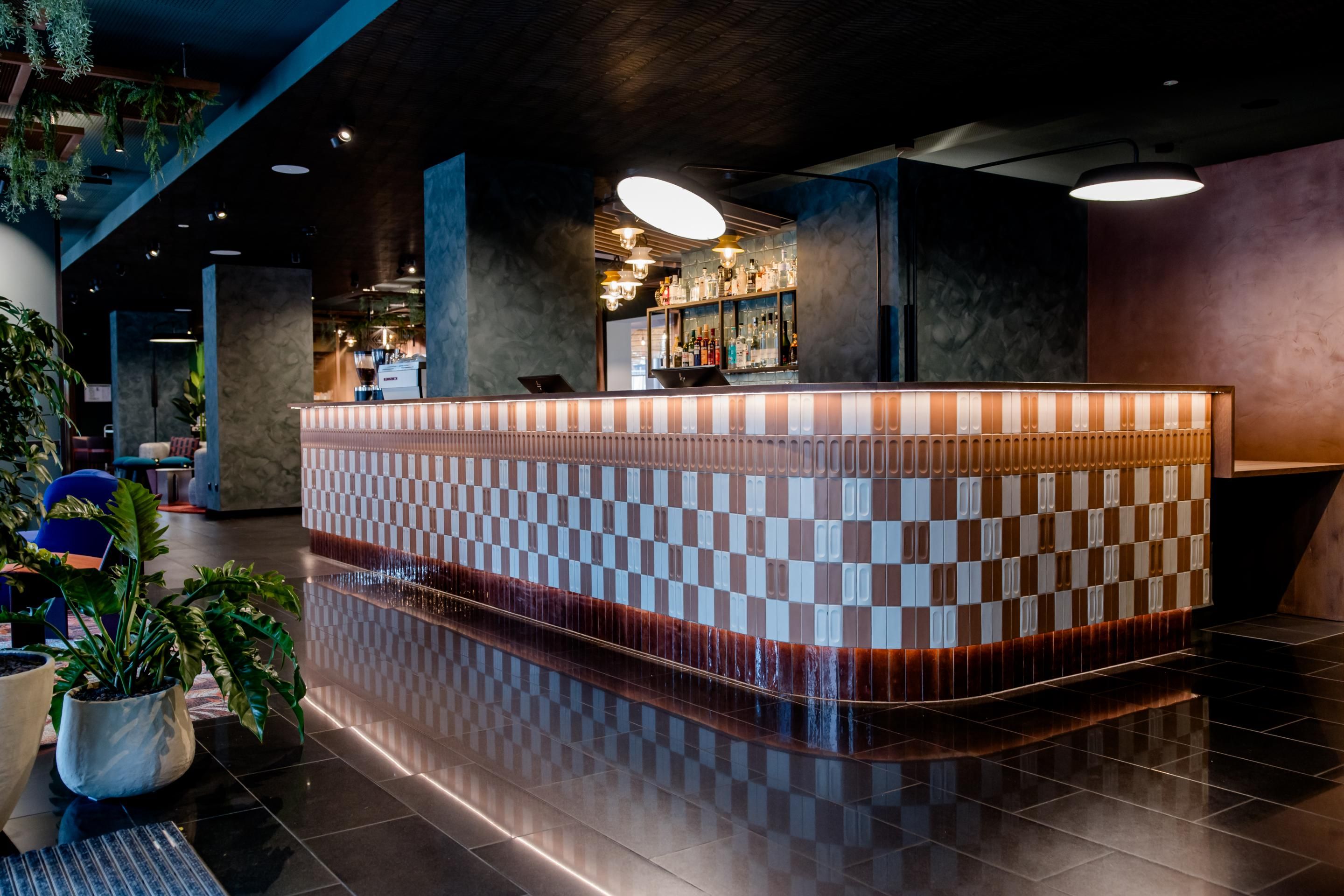 Moderner Hotel-Empfang mit stilvoll gestaltetem, beleuchtetem Tresen, dunklem Boden und Wänden sowie entspannter Atmosphäre für eine einladende Ankunft.