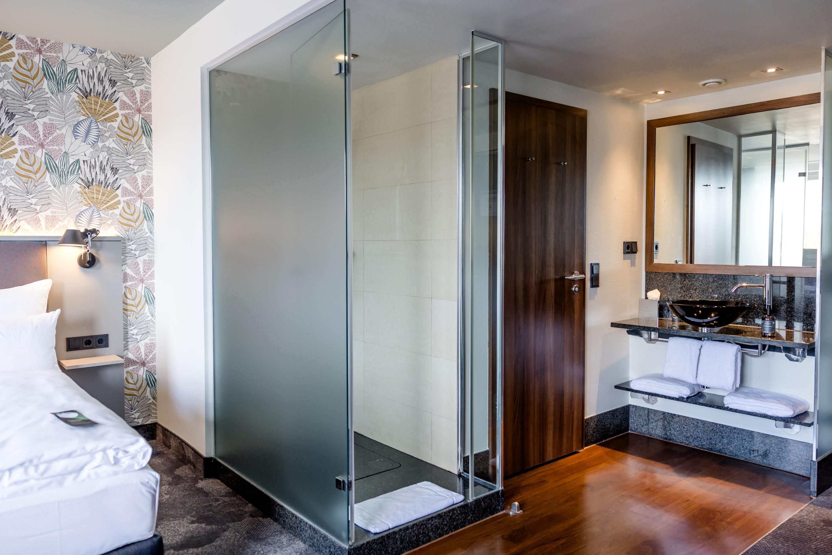 Modernes Hotelzimmer mit komfortablem Bett, separater Glasdusche, großem Spiegel und eleganter Badarmatur, helle und freundliche Atmosphäre.