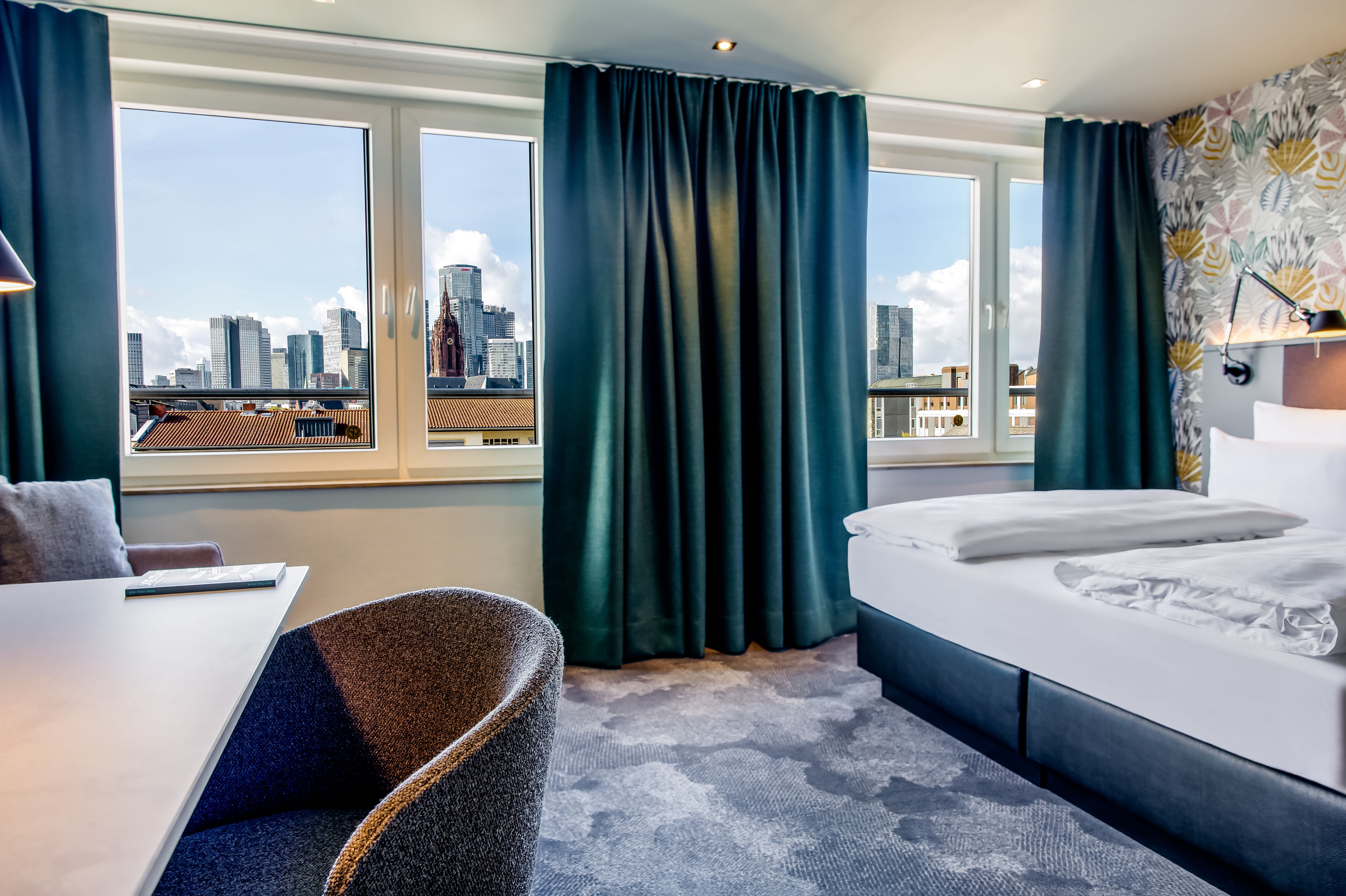 Modernes Hotelzimmer mit großem Fenster, das eine beeindruckende Stadtblick auf Wolkenkratzer bietet. Helle, freundliche Atmosphäre mit stilvoller Einrichtung und bequemen Betten, ideal für entspannte Aufenthalte in der Stadt.