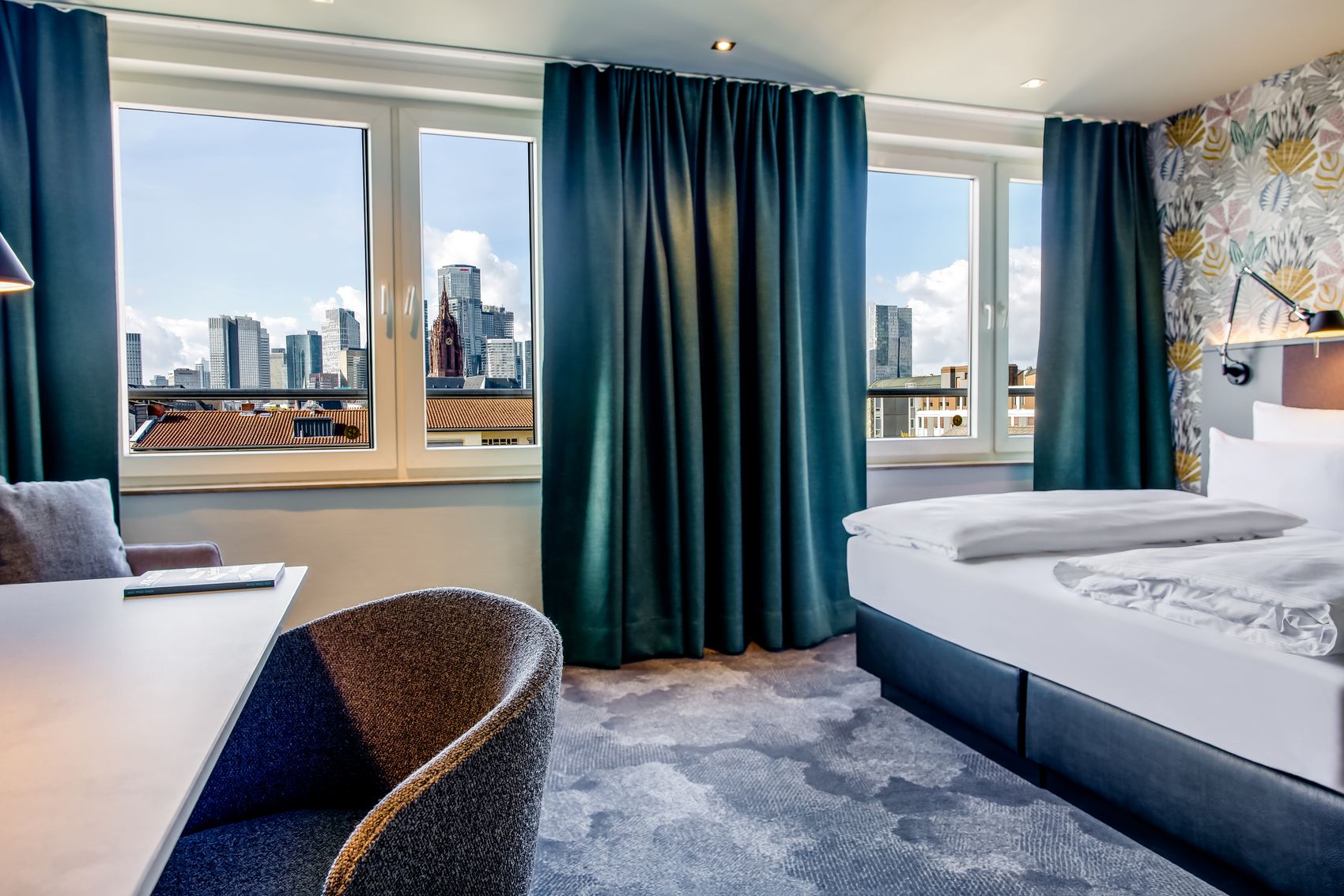 Modernes Hotelzimmer mit großem Fenster, das eine beeindruckende Stadtblick auf Wolkenkratzer bietet. Helle, freundliche Atmosphäre mit stilvoller Einrichtung und bequemen Betten, ideal für entspannte Aufenthalte in der Stadt.