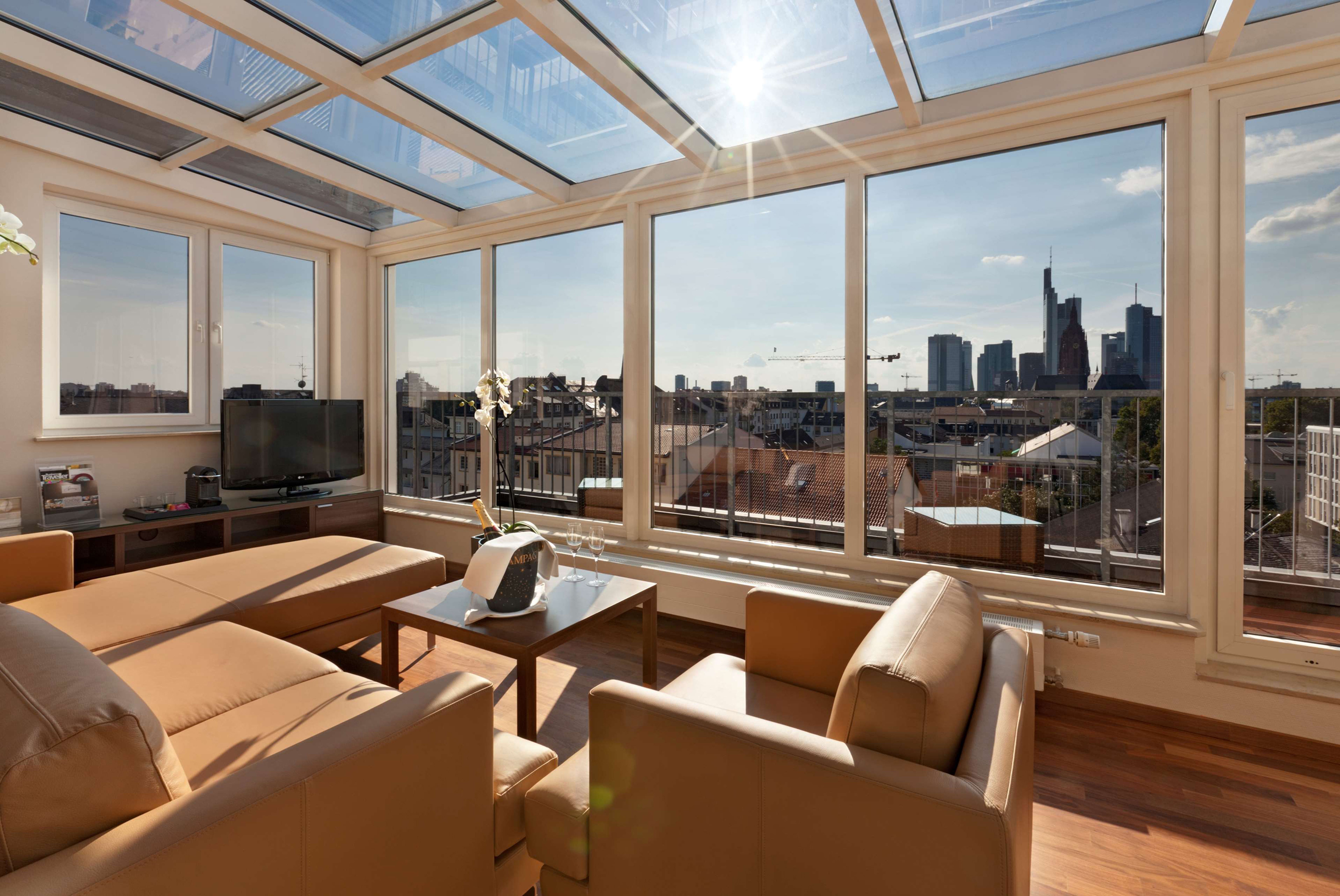 Helle Lounge mit bequemen Ledersesseln und -sofa, großflächigen Fenstern und Glasdach, die einen weiten Blick auf die Skyline der Stadt bieten. Sonnendurchfluteter Raum mit einladender Atmosphäre für entspannte Momente. Helle Lounge mit bequemen Ledersesseln und -sofa, großflächigen Fenstern und Glasdach, die einen weiten Blick auf die Skyline der Stadt bieten. Sonnendurchfluteter Raum mit einladender Atmosphäre für entspannte Momente.