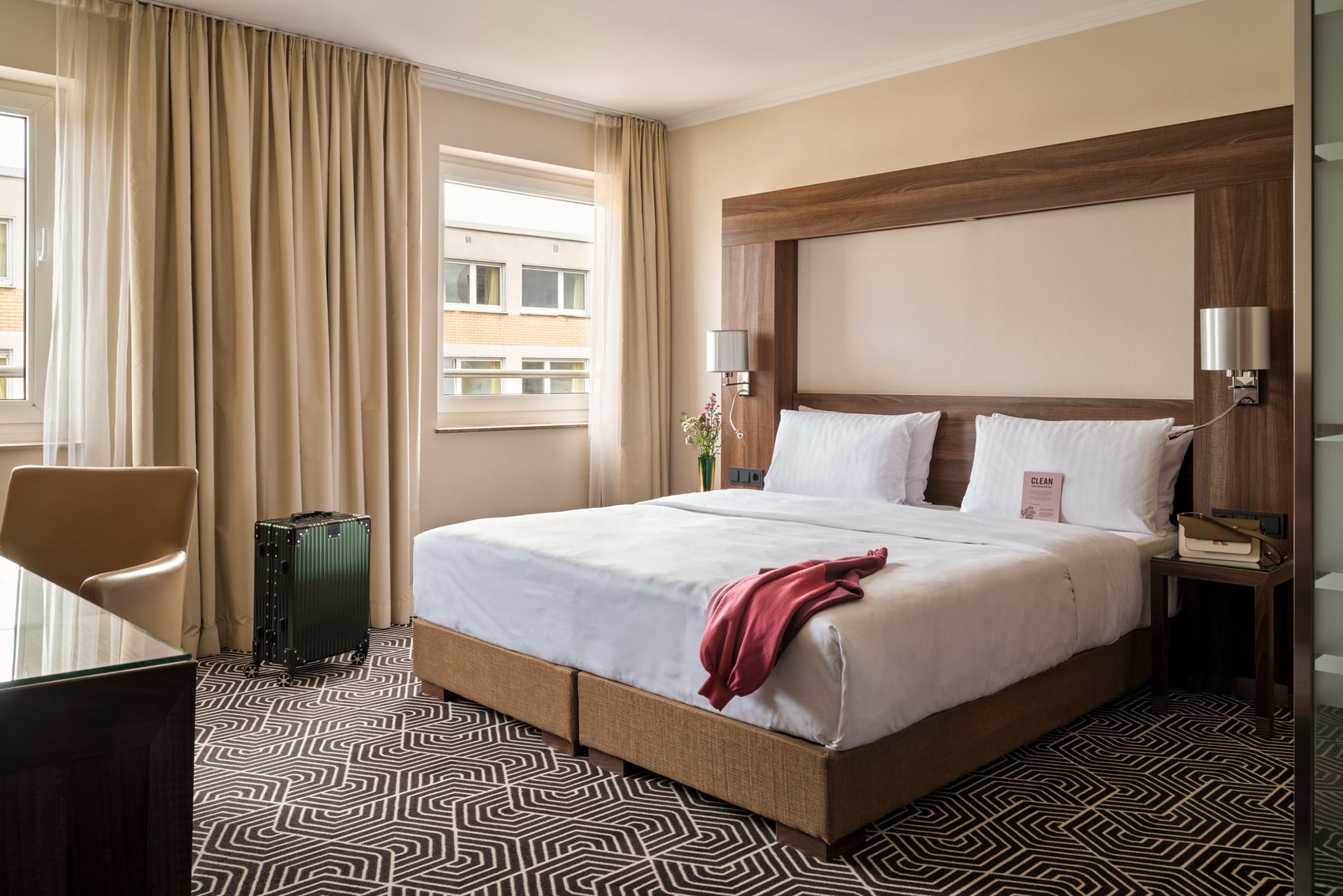 Komfortables Hotelzimmer mit großem Doppelbett, stilvollem Holzrahmen, weichen Vorhängen, Teppichboden in modernem Muster und ruhiger Atmosphäre, ideal für erholsamen Aufenthalt.