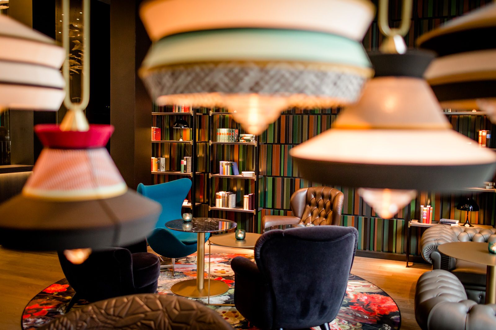 Designhotel Frankfurt Römer Motel One helle Lounge mit mehreren Sesseln, farbenfrohen Lampen sowie Bücherregalen