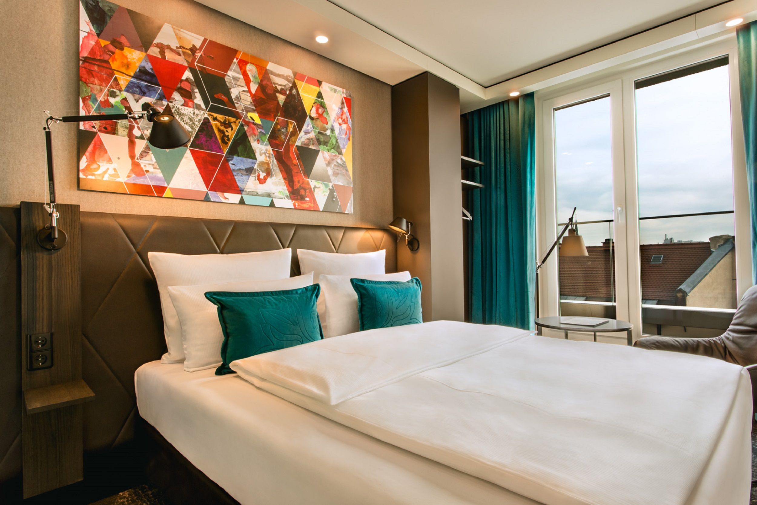 Designhotel Frankfurt Römer Motel One Zimmer mit Doppelbett, farbenfrohem Gemälde an der Wand sowie bodentiefem Fenster