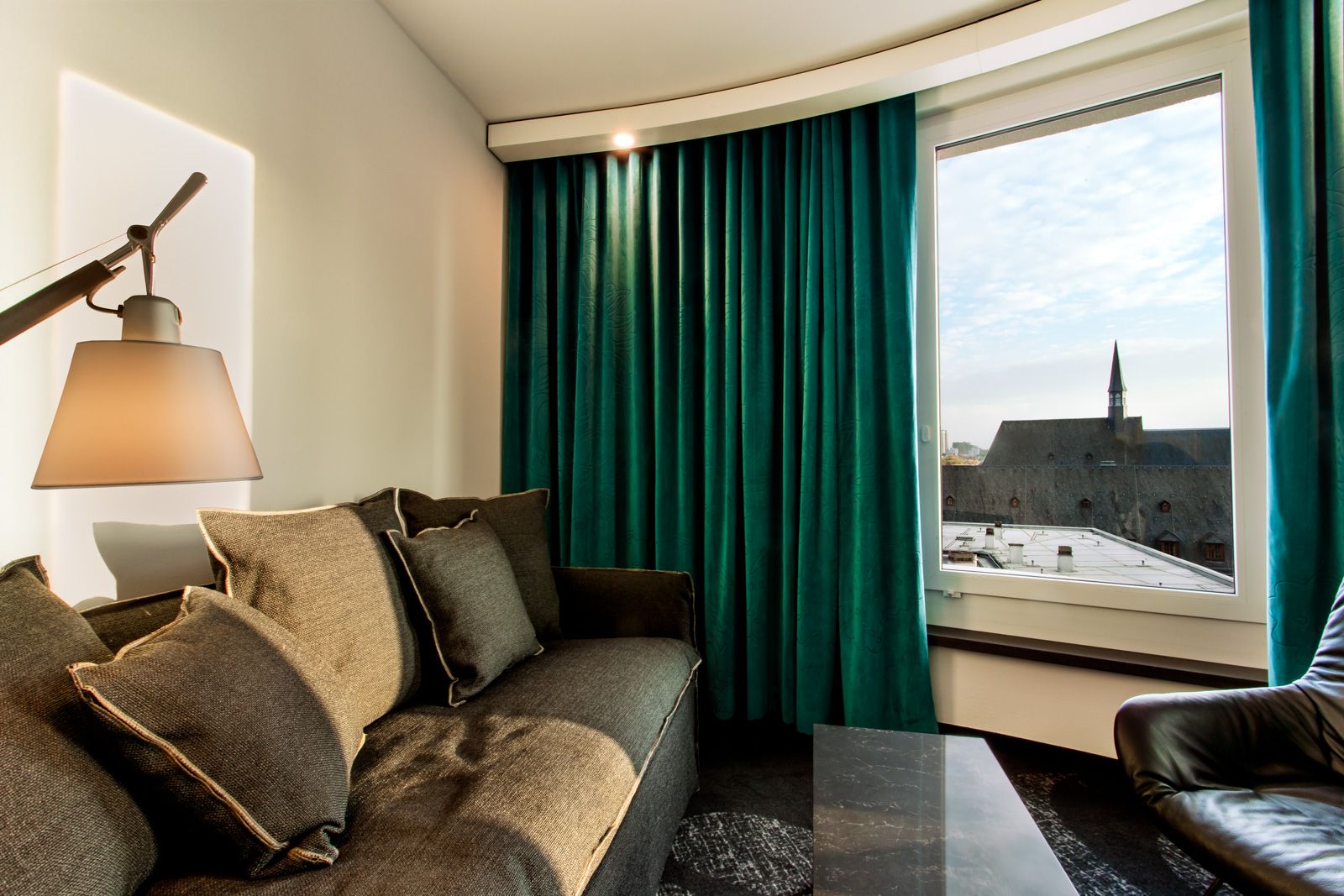 Designhotel Frankfurt Römer Motel One Zimmer mit großem Sofa und Sessel sowie Ausblick über die Dächer der Stadt