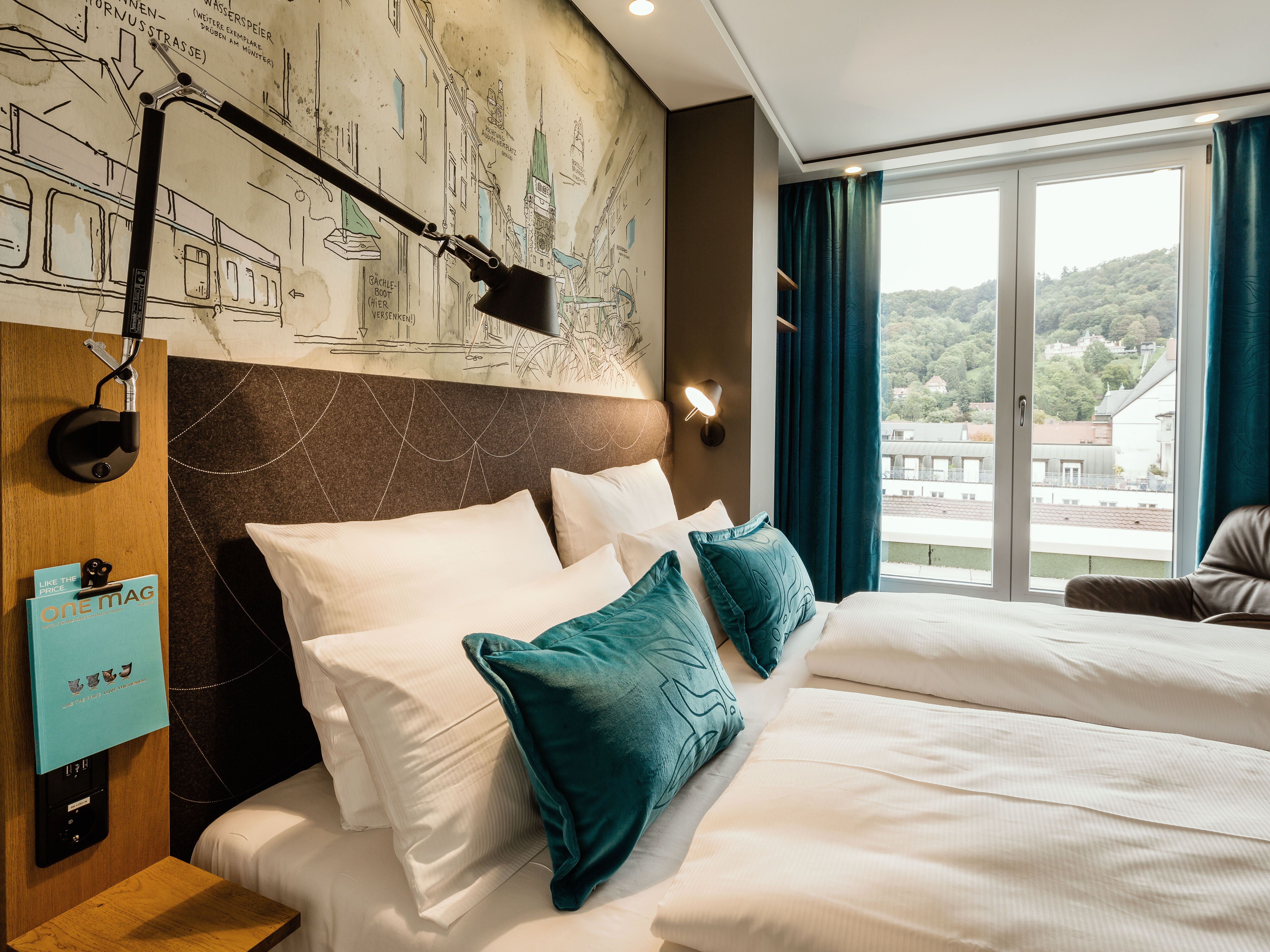 Hotel Freiburg Motel One seitlicher Blick über geräumiges Doppelbett durch ein bodentiefes Fenster