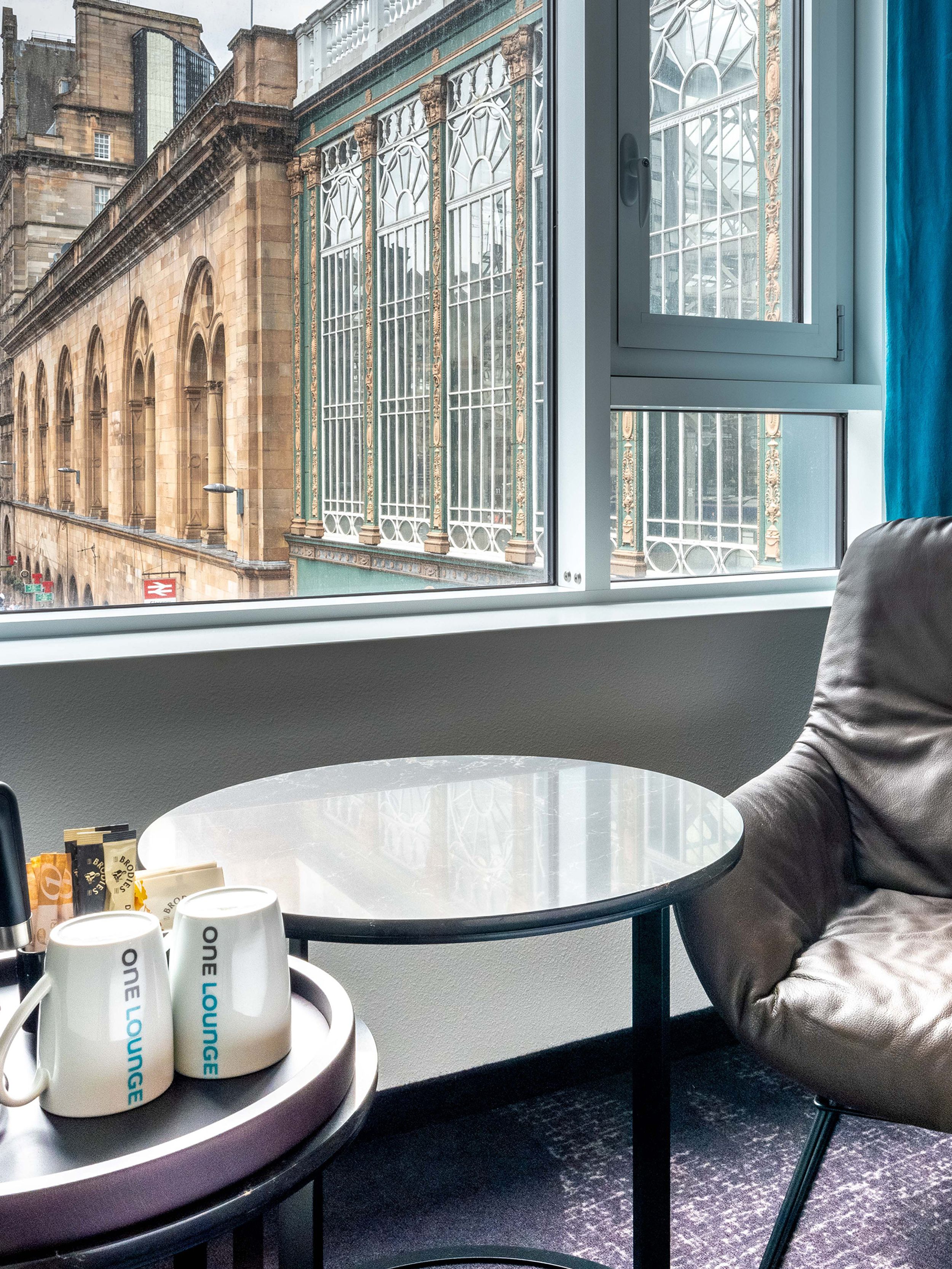 Hotel Glasgow Motel One Zimmer mit Sessel, Beistelltisch, Wasserkocher und zwei Tassen vor großem Fenster