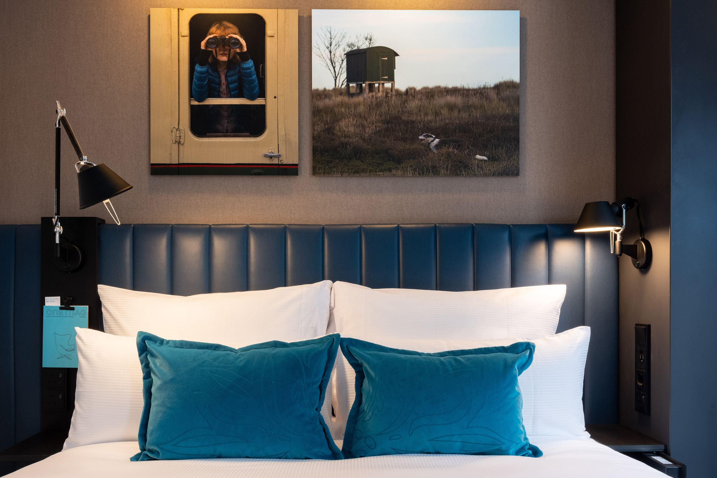Hotel Glasgow Motel One Blick auf großes Doppelbett mit zwei Zierkissen in türkis sowie zwei Bilder an der Wand