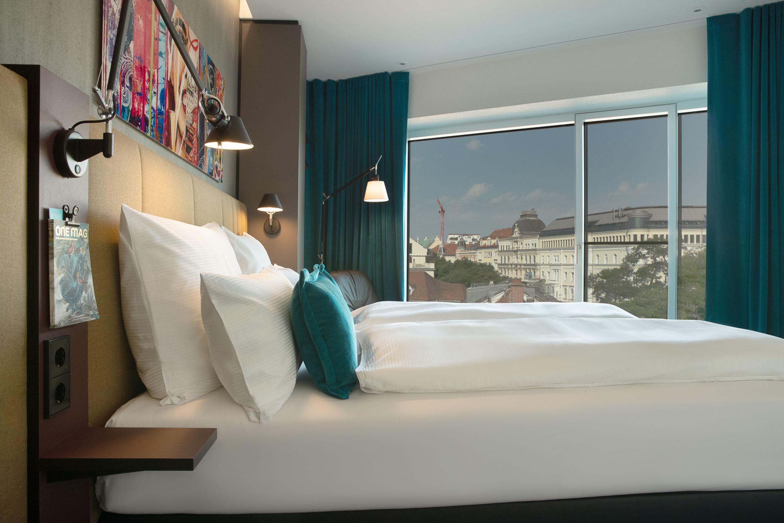 Hotel Graz Motel One seitlicher Blick auf Doppelbett sowie großes bodentiefes Fenster