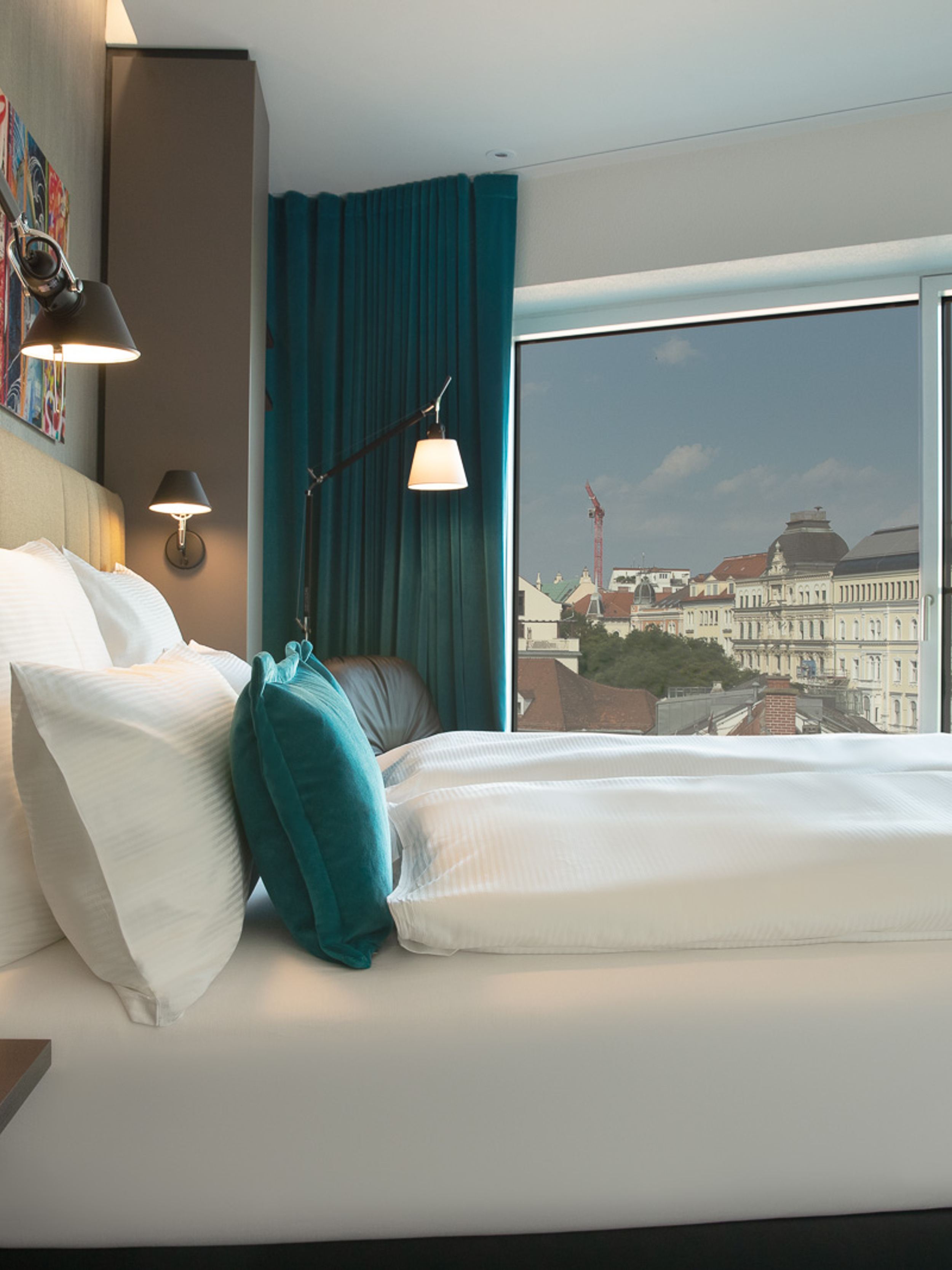 Hotel Graz Motel One seitlicher Blick auf Doppelbett sowie großes bodentiefes Fenster