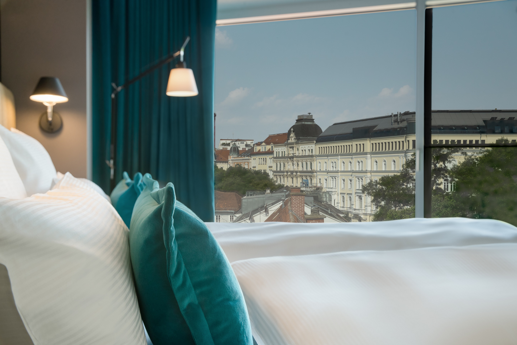 Hotel Graz Motel One Zimmer mit geräumigem Doppelbett sowie bodentiefem Fenster mit Stadtblick
