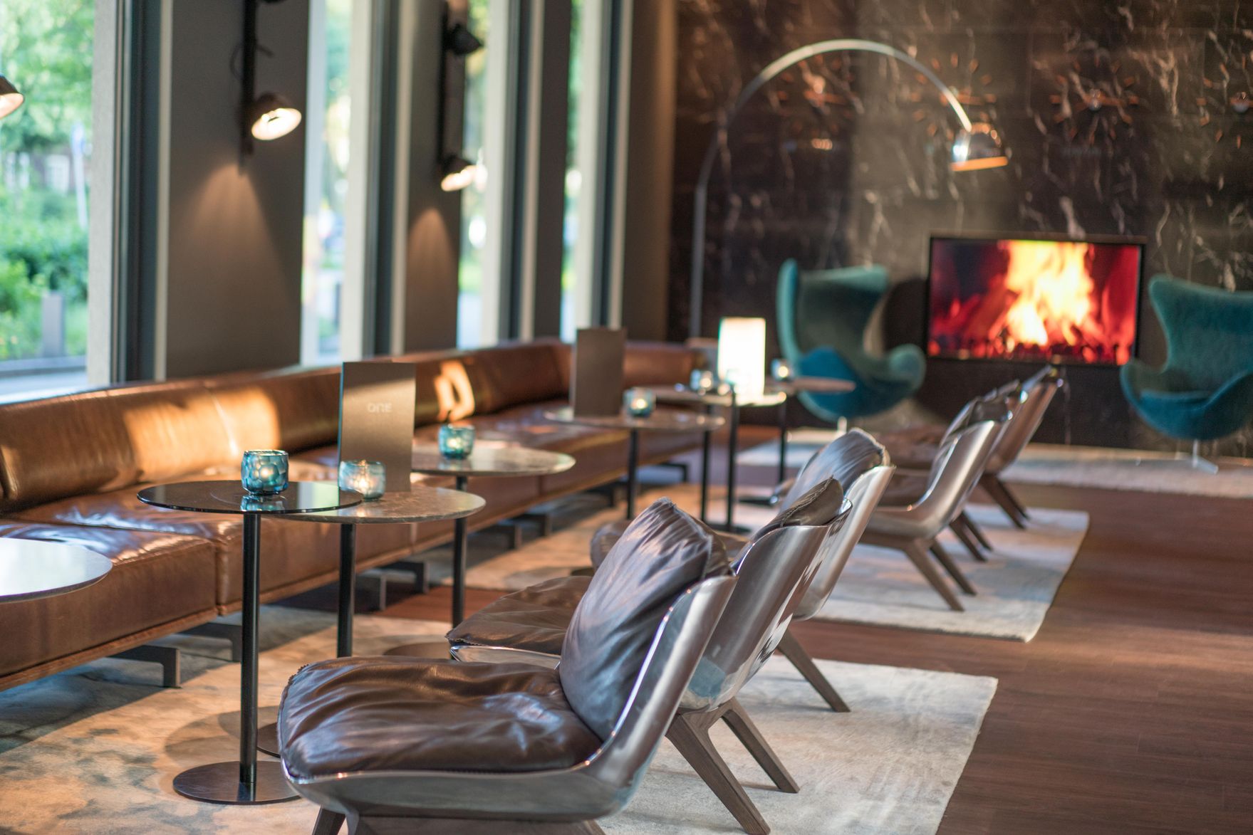 Hotel Hamburg Airport Motel One Lounge mit mehreren Tischen und Stühlen sowie Egg chair und TV im Hintergrund