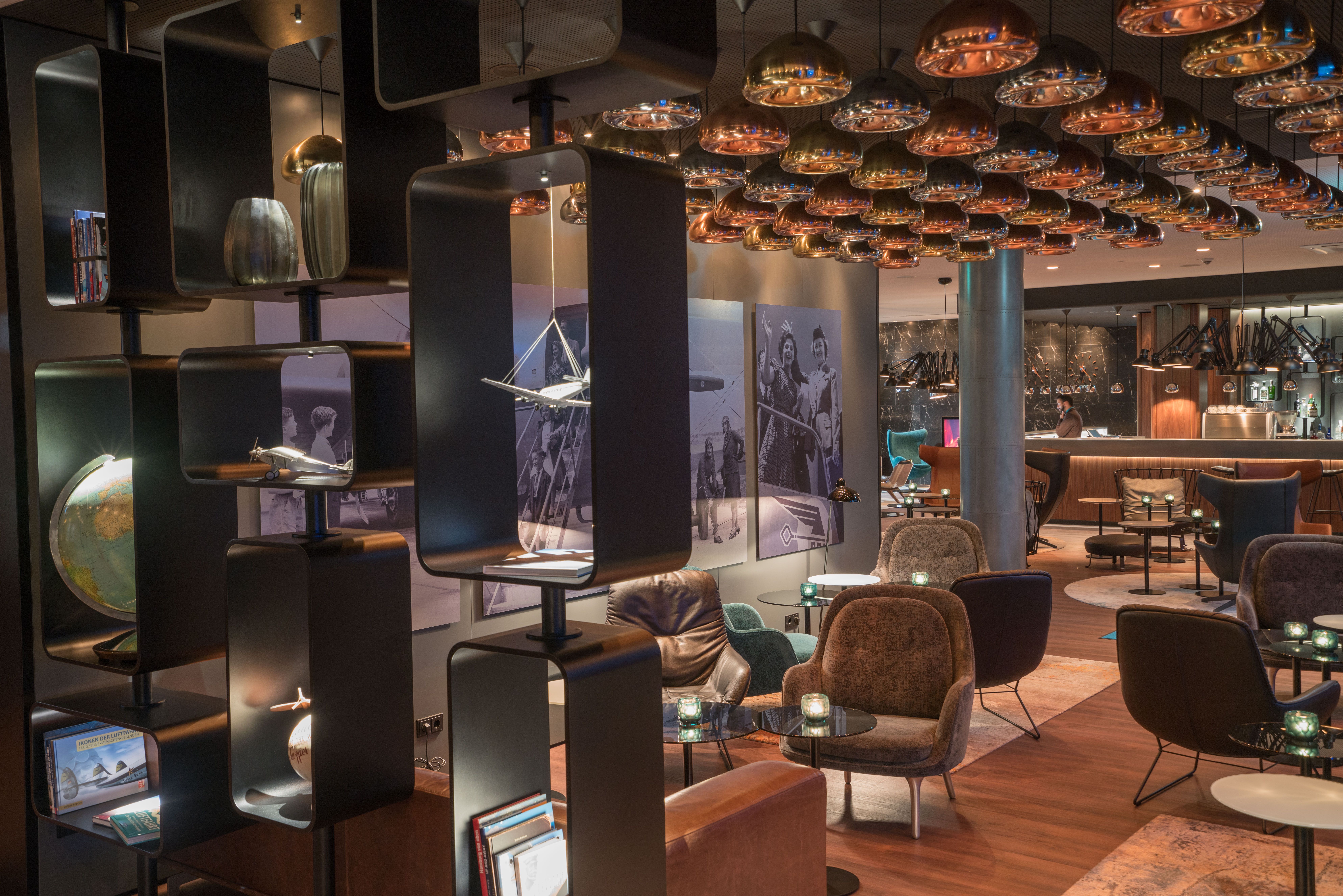 Hotel Hamburg Airport Motel One große Lounge mit mehreren Sitzgelegenheiten sowie Rezeption mit Mitarbeiter im Hintergrund