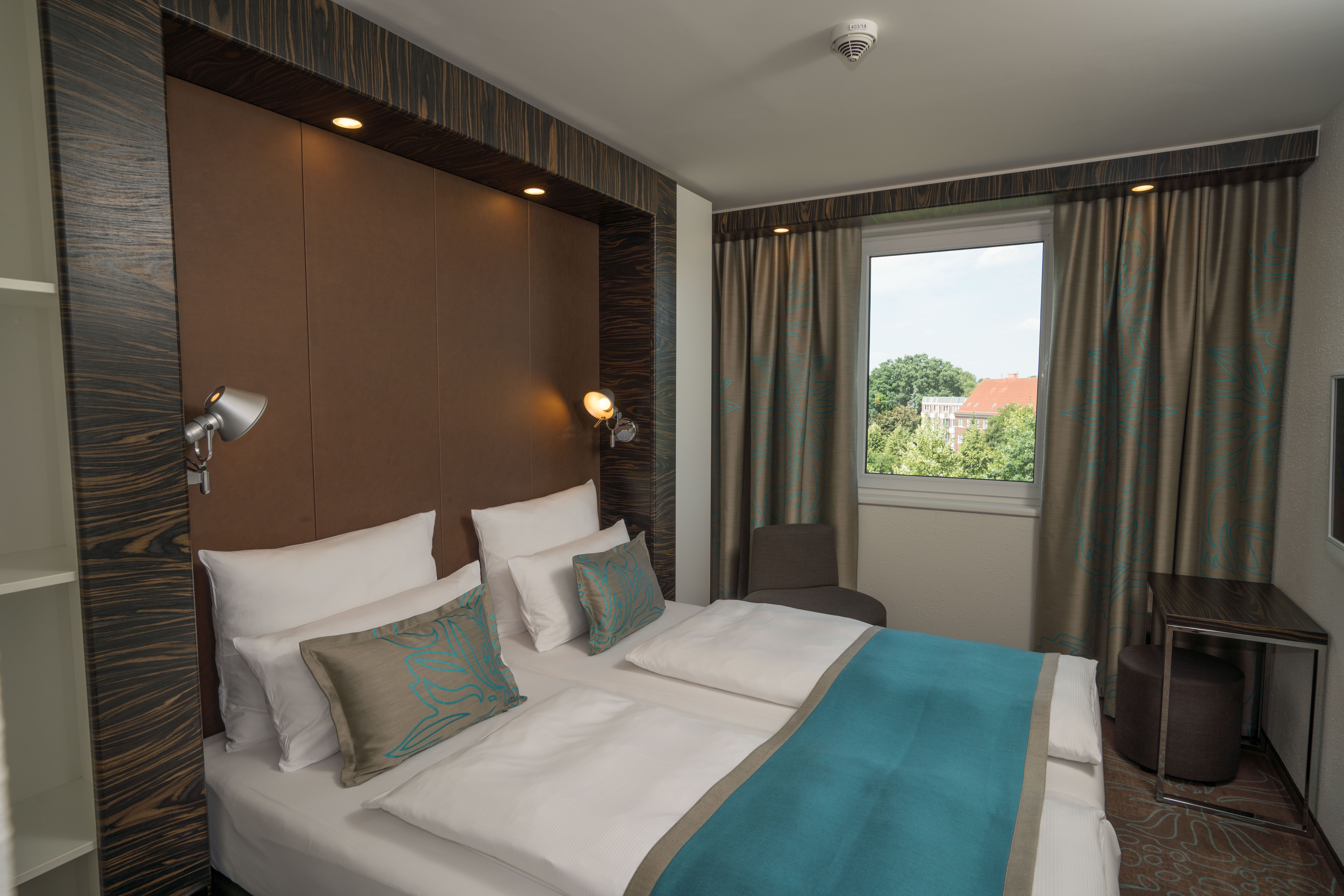 Hotel Hamburg Airport Motel One Blick auf geräumiges Doppelbett mit Sessel in der Ecke und einem Tisch