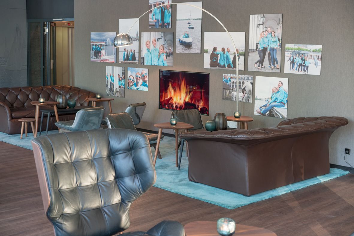 hotel Hamburg Alster Motel One bright lounge with sofas and armchairs and a large TV on the wall showing fire