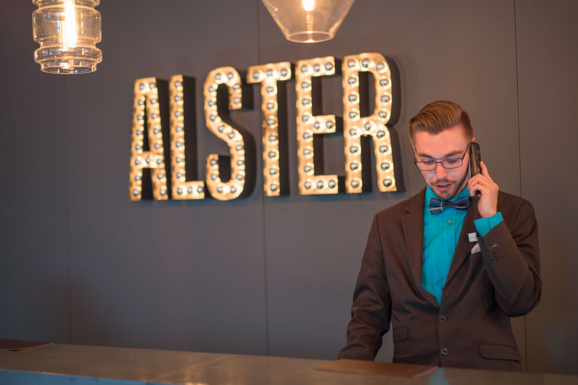 designhotel Hamburg Alster Motel One staff on the phone at reception and “Alster” lettering on the wall
