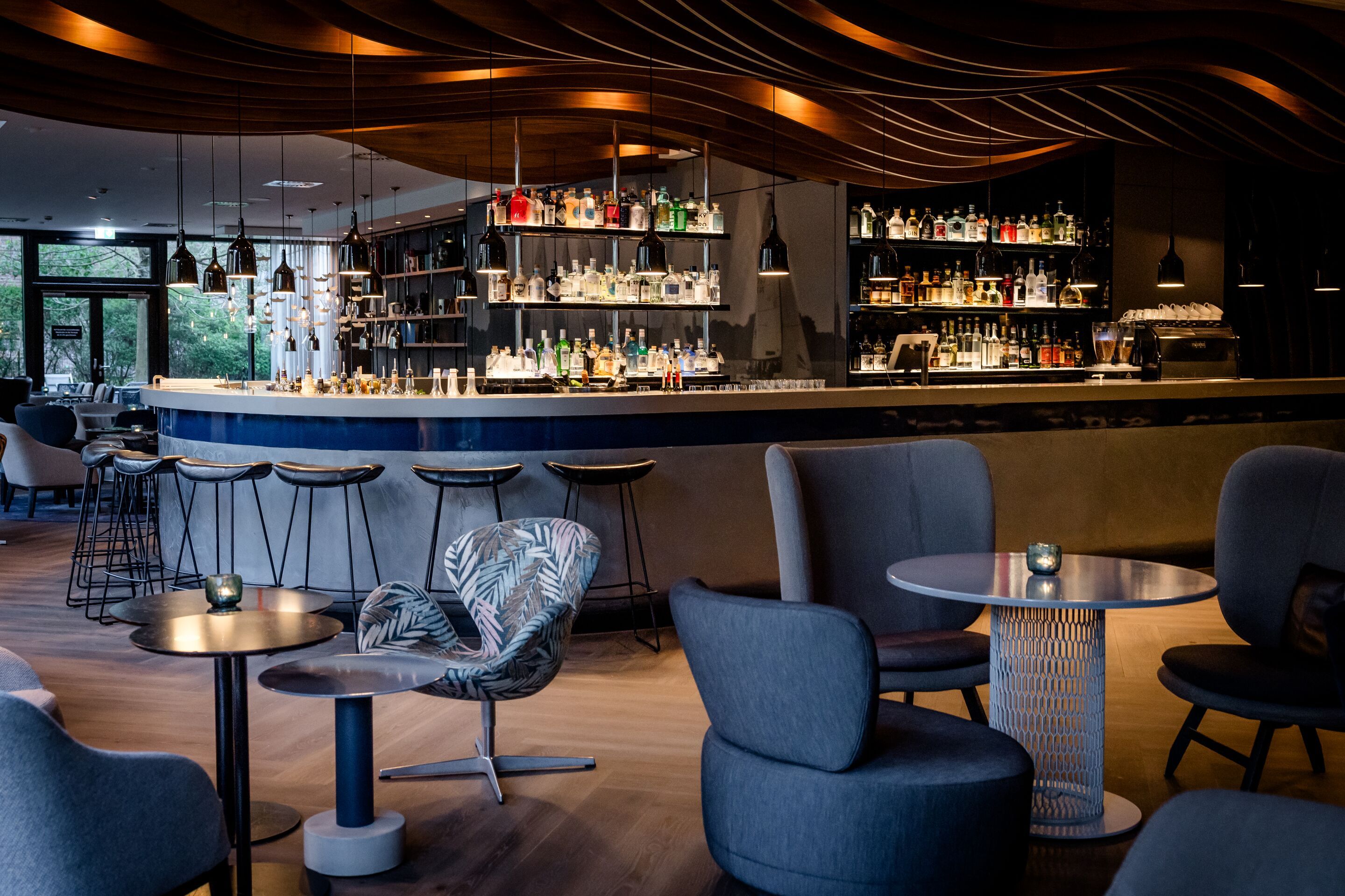 Hotel Hamburg-Alster Motel One Lounge und Bar mit stilvoller Beleuchtung, langem Tresen, einer großen Auswahl an Spirituosen und gemütlichen Sitzbereichen mit Polstersesseln.