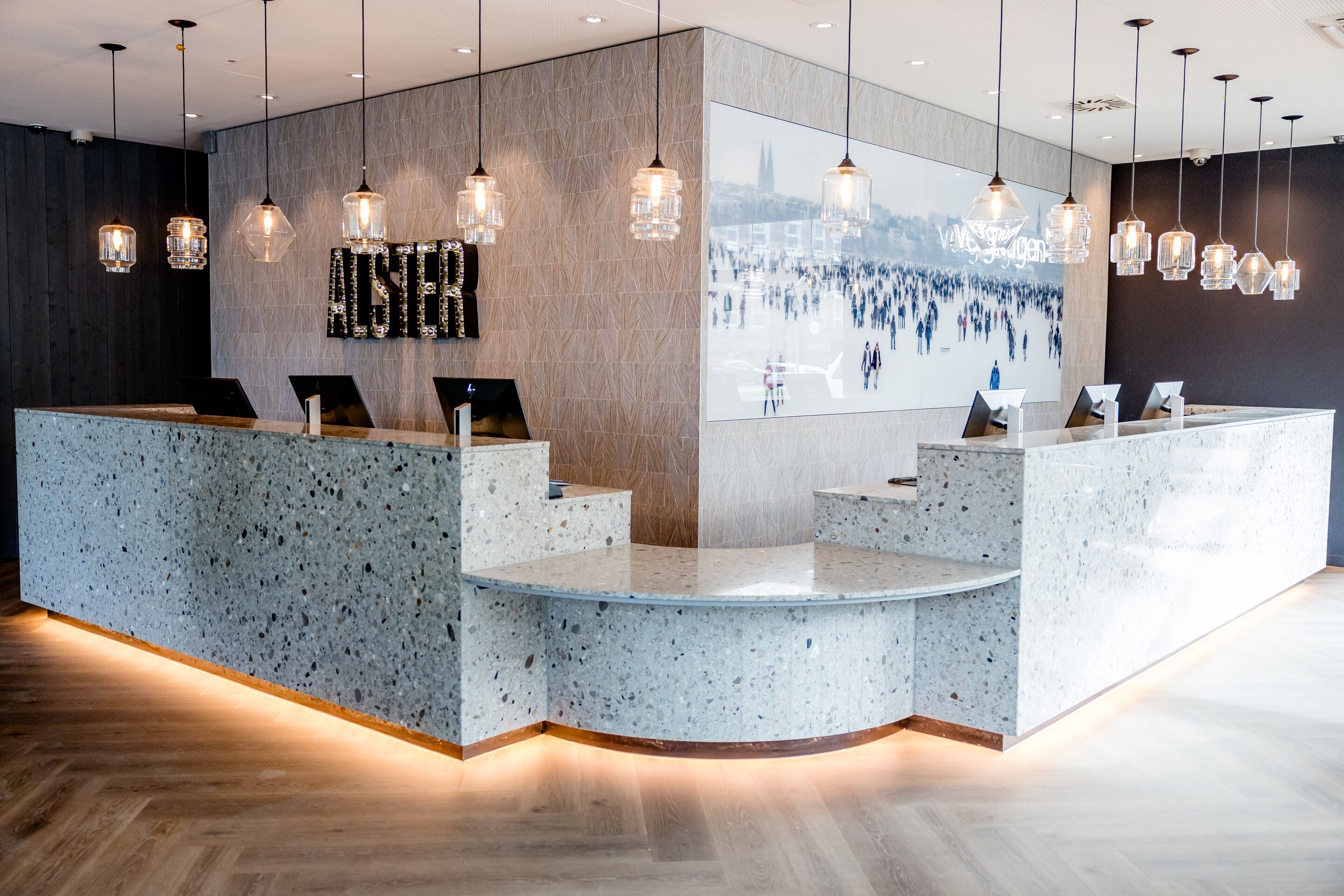 Hotel Hamburg-Alster Motel One Empfangsbereich mit marmoriertem Tresen, mehreren Computern und stilvollen Hängelampen.