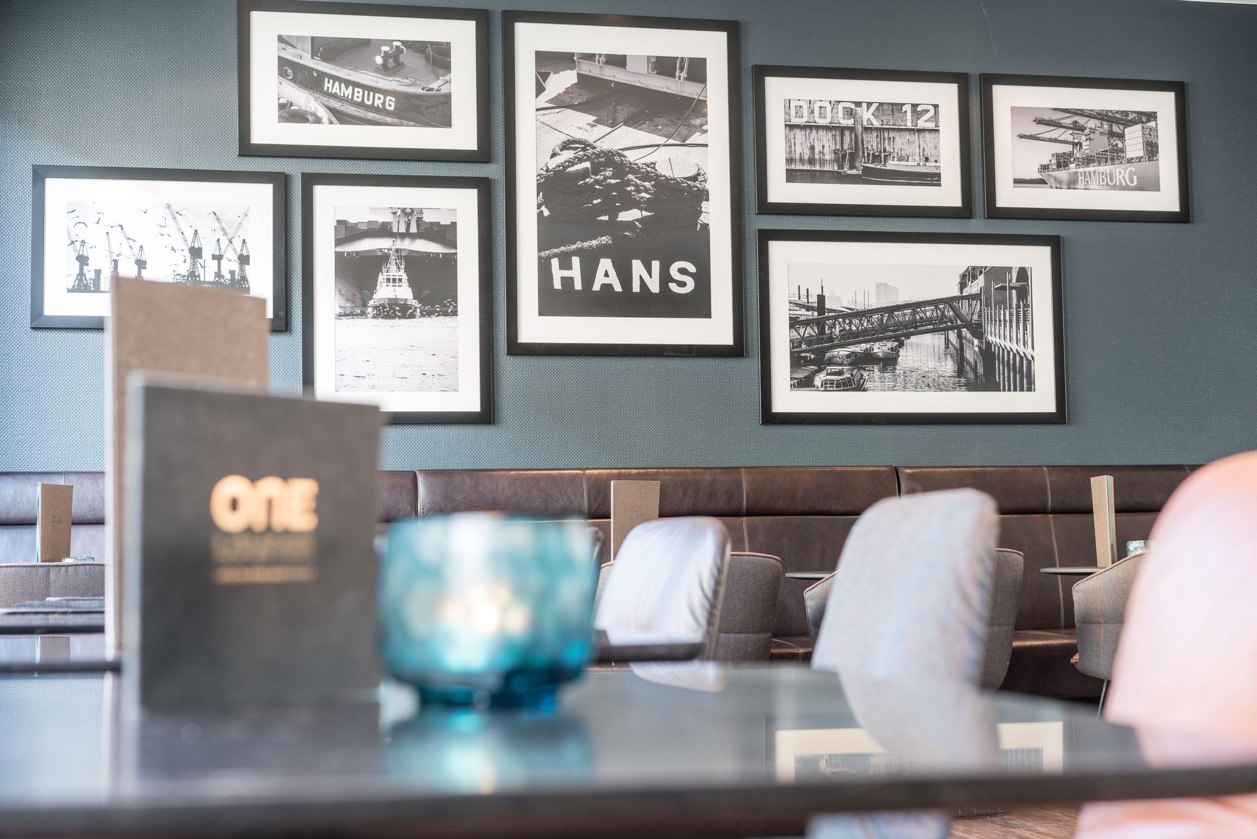 Hotel Hamburg Altona Motel One Nahaufnahme über einen Tisch auf weitere Tische sowie eine Wand mit mehreren Bildern