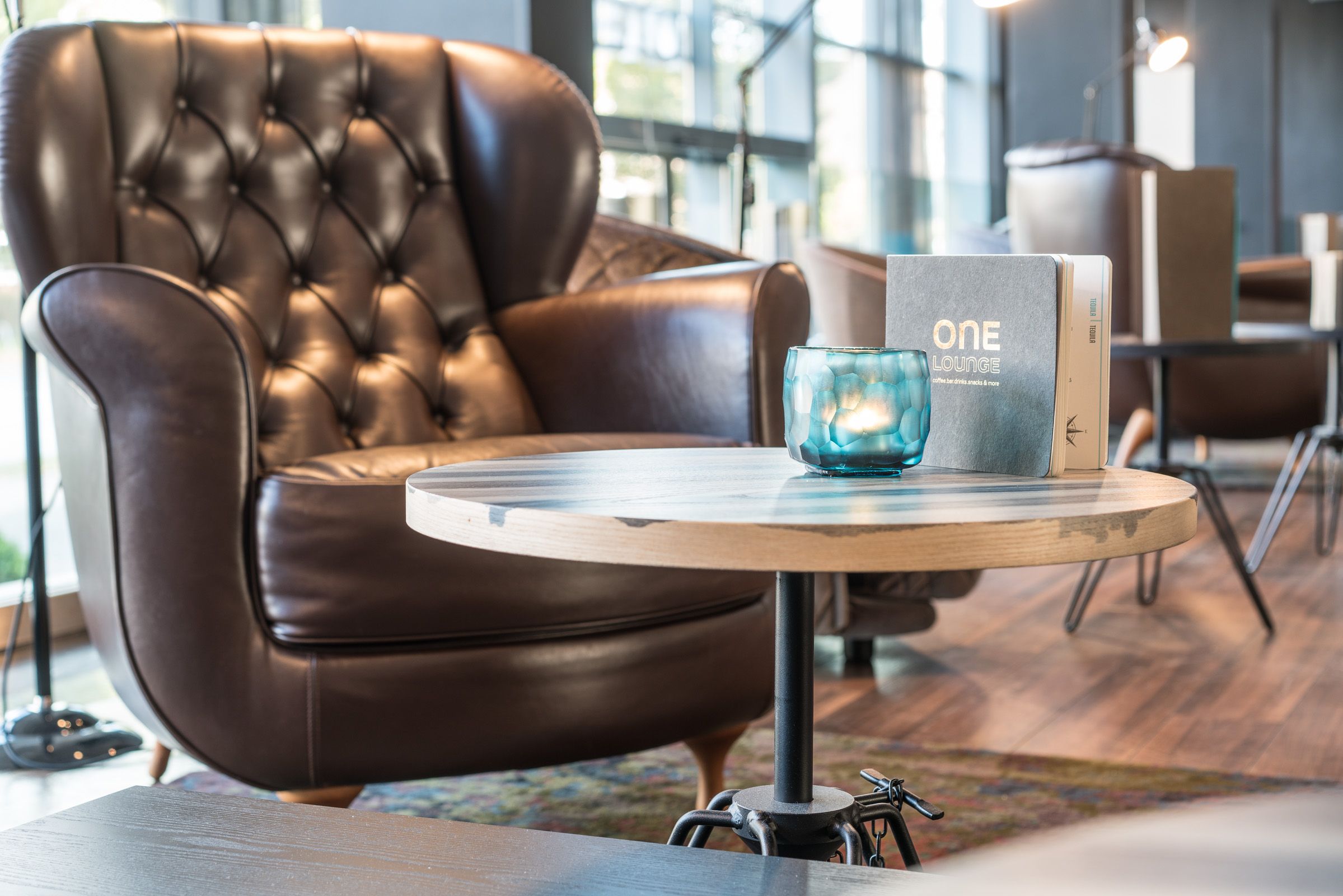 Designhotel Hamburg Altona Motel One Sessel mit Beistelltisch, auf dem eine Getränkekarte sowie eine Kerze steht