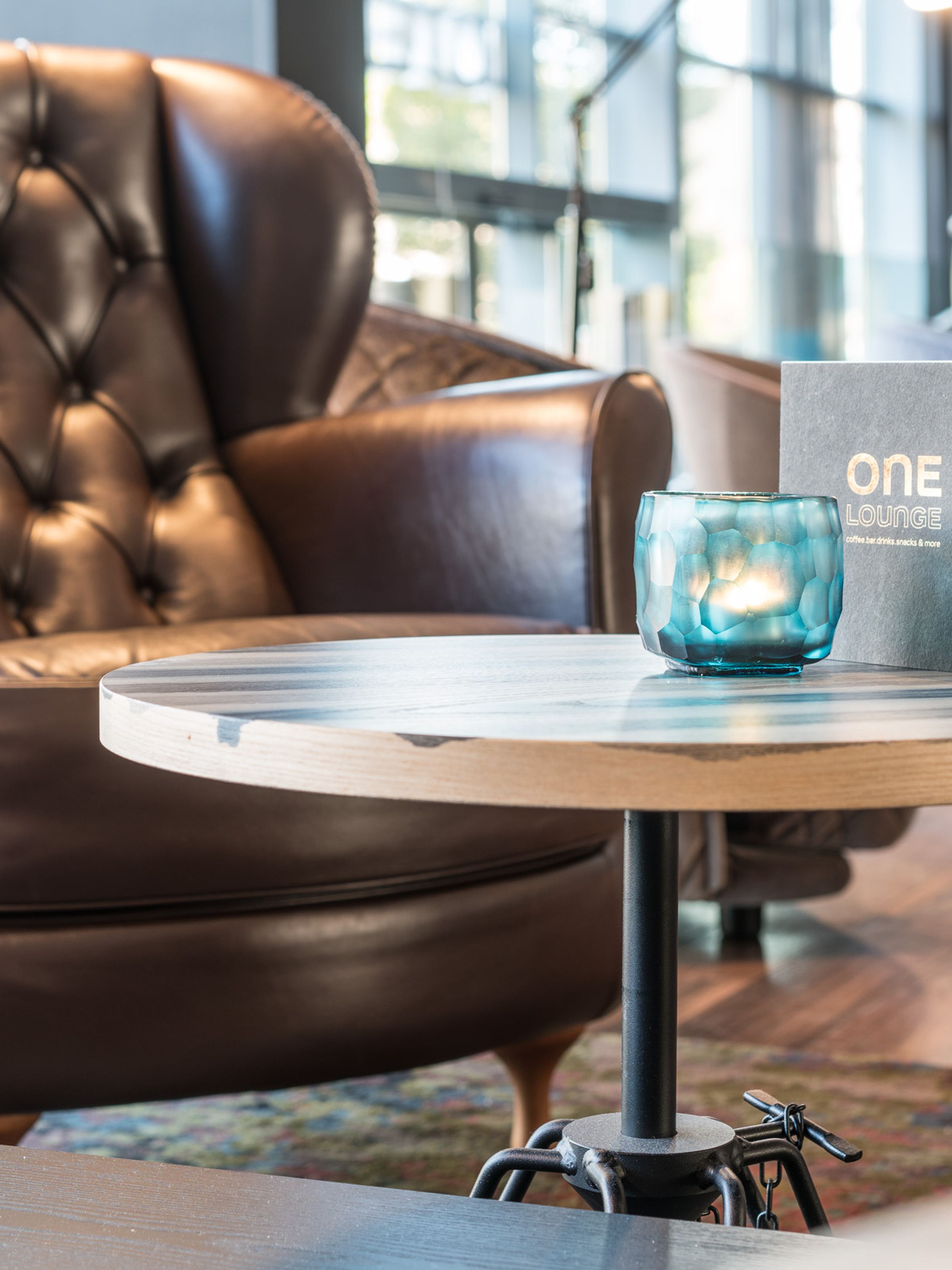 Designhotel Hamburg Altona Motel One Sessel mit Beistelltisch, auf dem eine Getränkekarte sowie eine Kerze steht