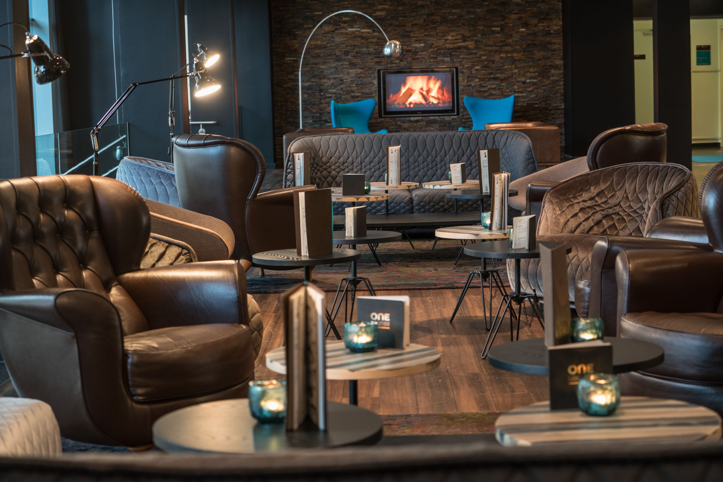 Hotel Hamburg Altona Motel One Lounge mit Sesseln und Sofas sowie einem Fernseher an der Wand