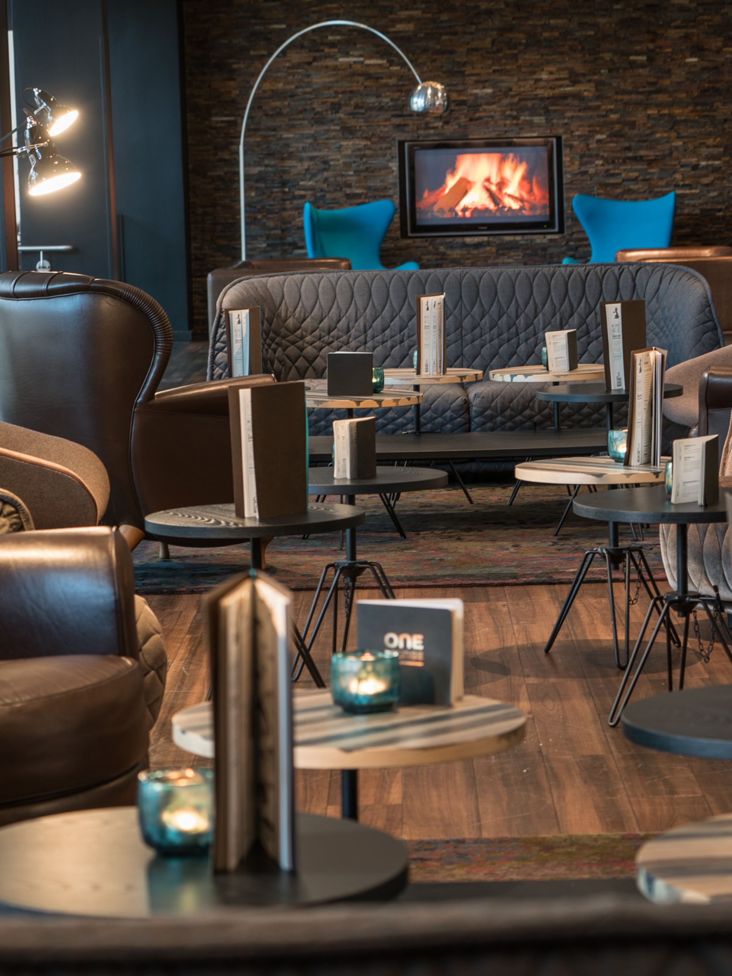 Hotel Hamburg Altona Motel One Lounge mit Sesseln und Sofas sowie einem Fernseher an der Wand