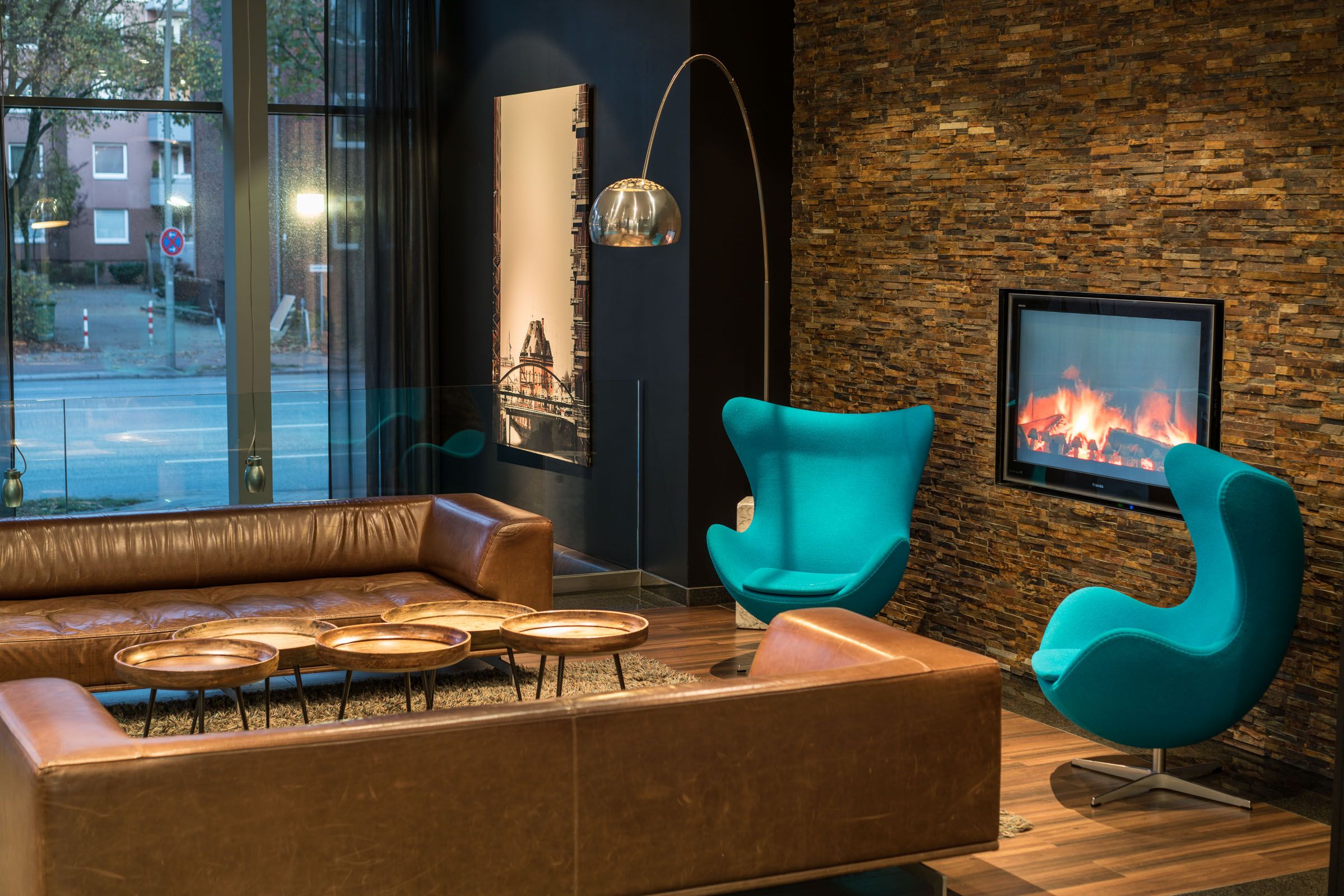 Hotel Hamburg Altona Motel One Lounge mit großen Sofas sowie zwei Egg chairs und Fernseher an der Wand