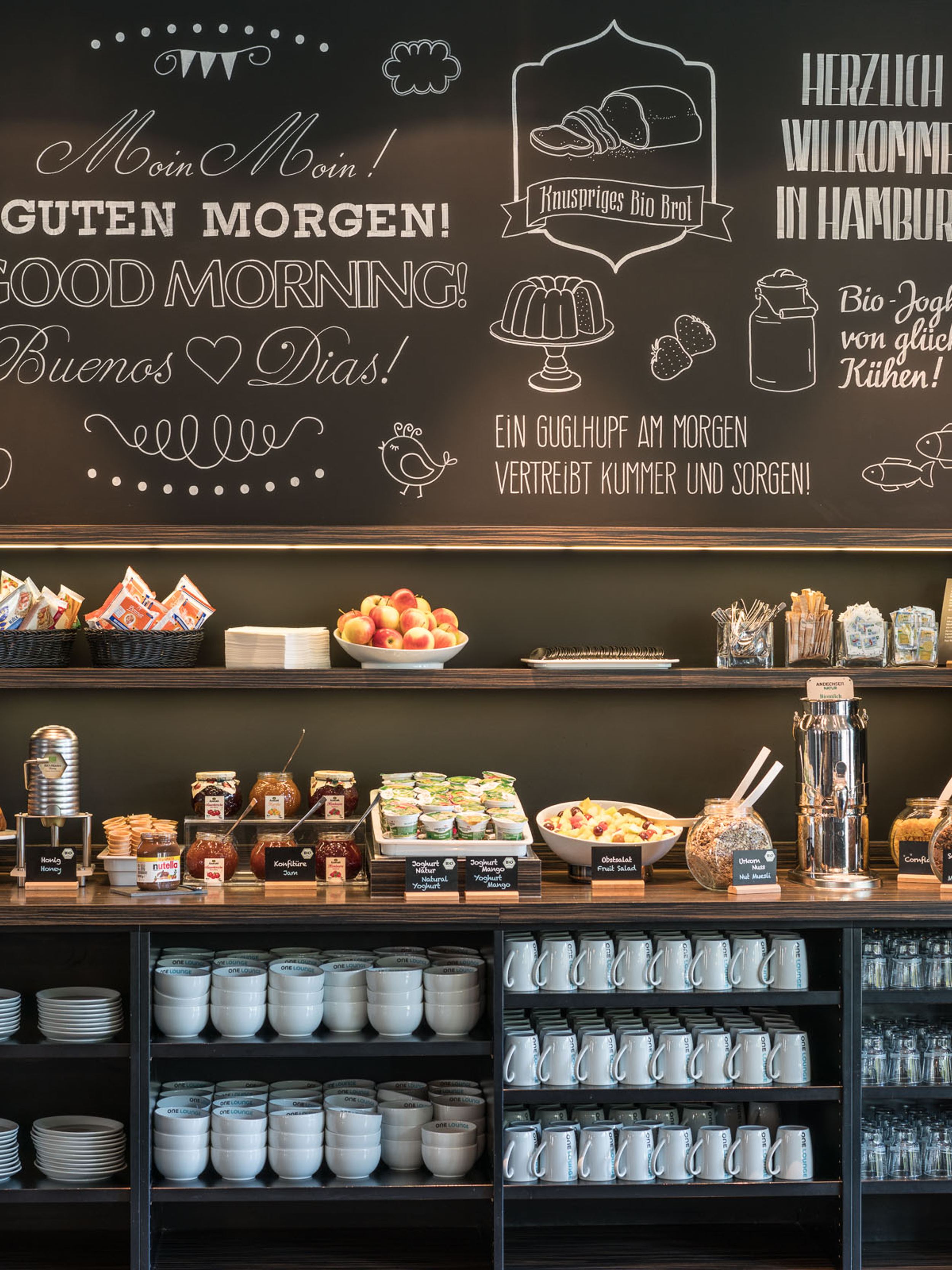 Hotel Hamburg Altona Motel One Frühstücksbuffet mit großer Auswahl an Essen und Getränken sowie Geschirr