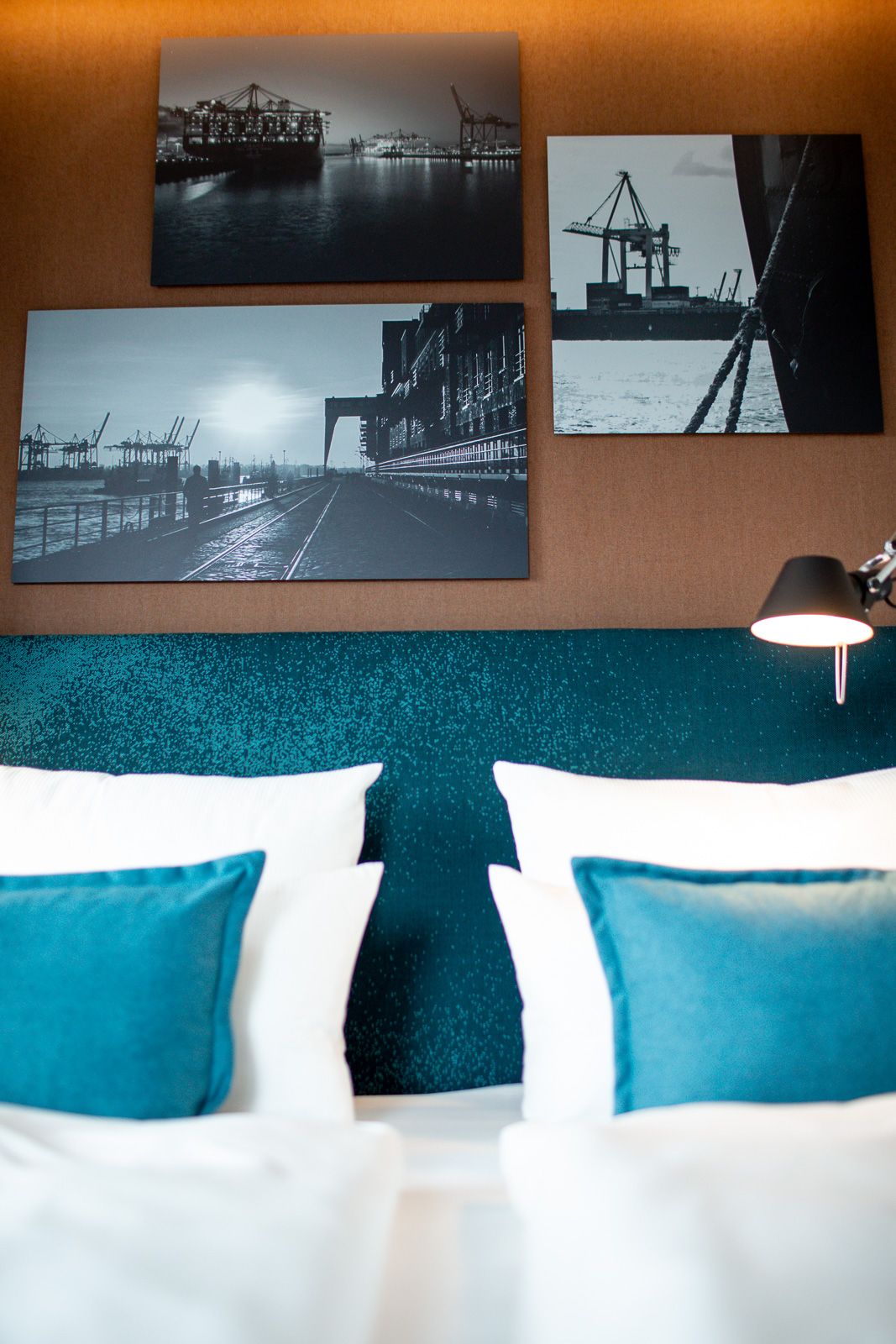 Hotel Hamburg Fleetinsel Motel One Zimmer mit Blick auf das Kopfteil eines Doppelbettes mit Zierkissen in türkis und drei Bildern an der Wand