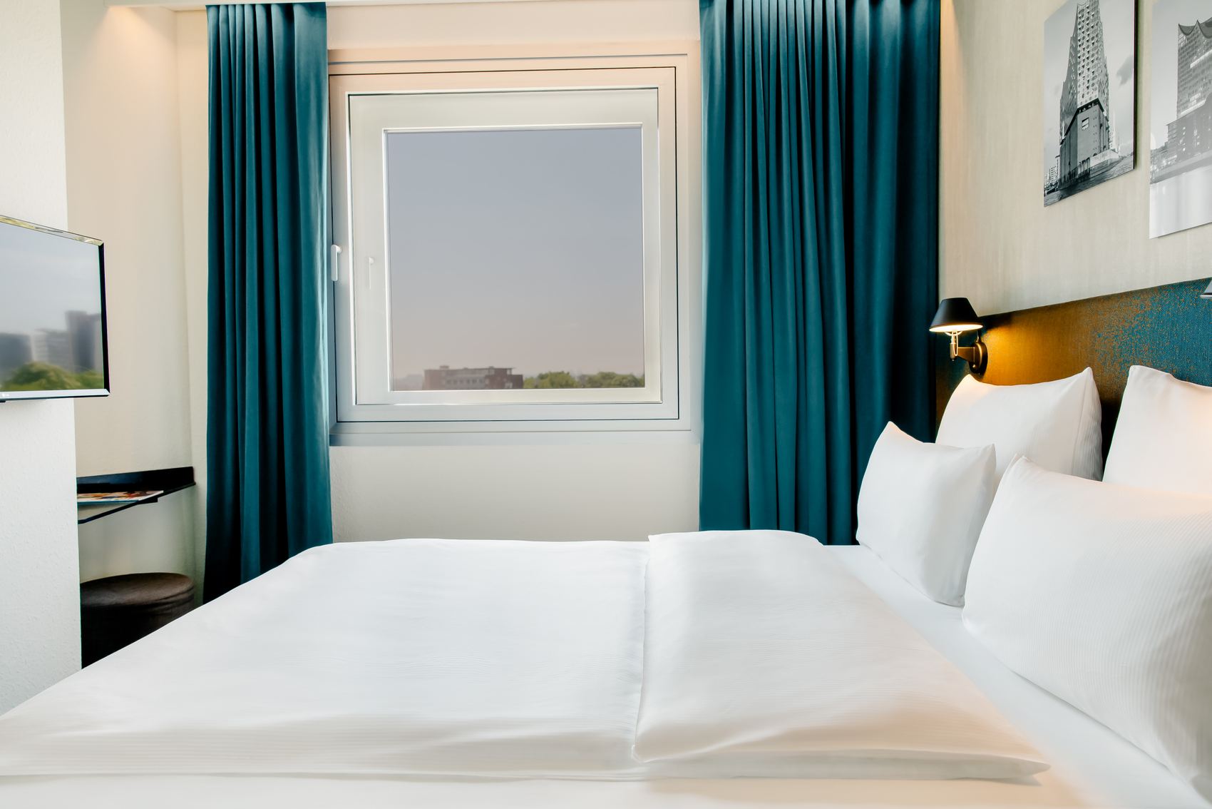 Helles, modernes Hotelzimmer mit großem, bequemem Doppelbett, weißen Bettwäsche, Fenster mit Blick nach draußen und dunkelblauen Vorhängen, das eine gemütliche und ruhige Atmosphäre für erholsamen Aufenthalt schafft.