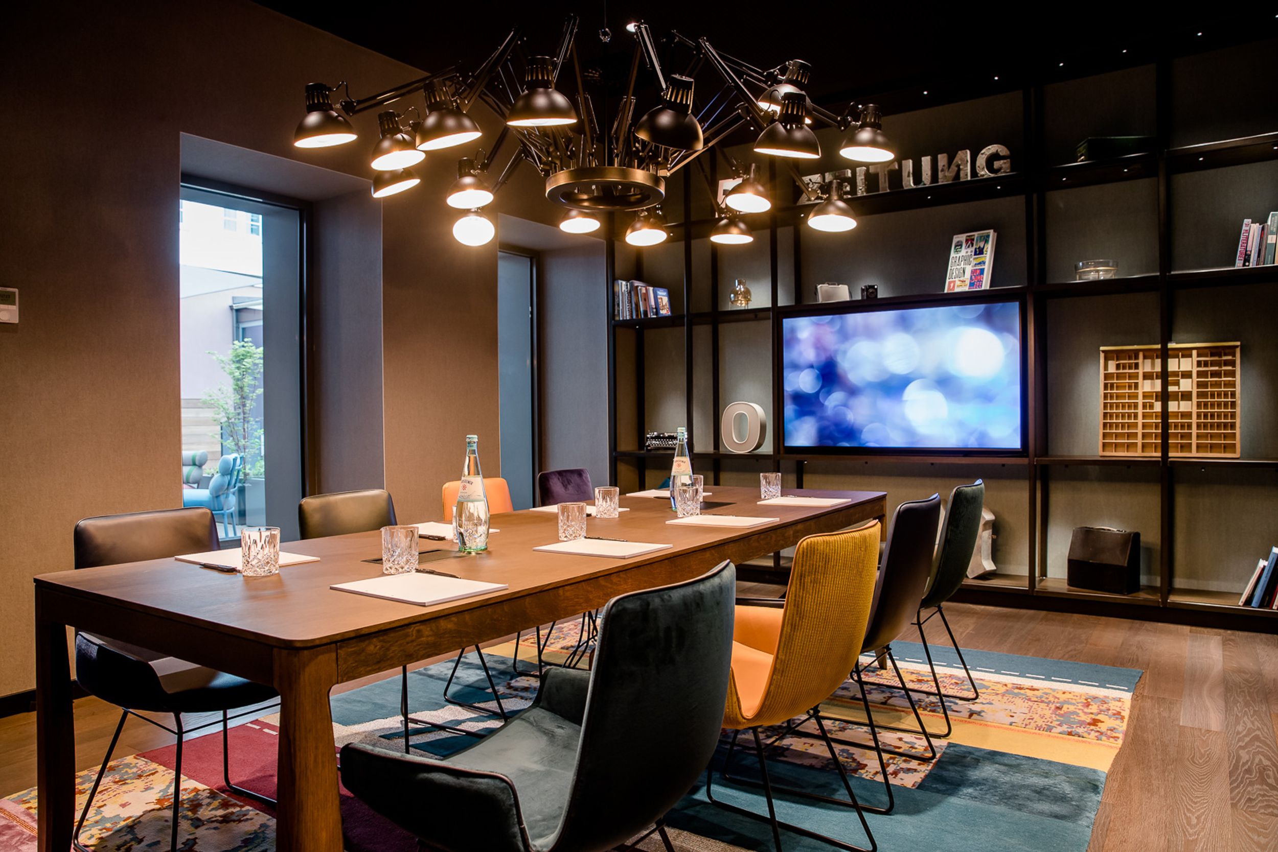Designhotel Hannover Oper Motel One Meetingraum mit Tisch, acht Stühlen und Fernseher an der Wand