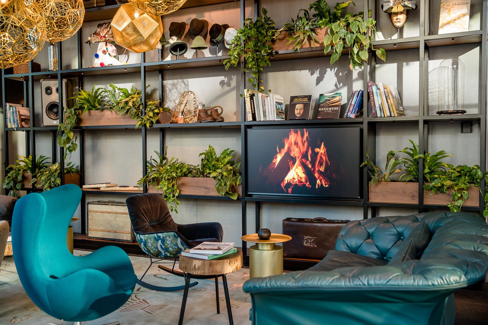 Designhotel Innsbruck Motel One Egg chair und Sofa vor offenem Regal mit Fernseher an der Wand, der ein Lagerfeuer zeigt