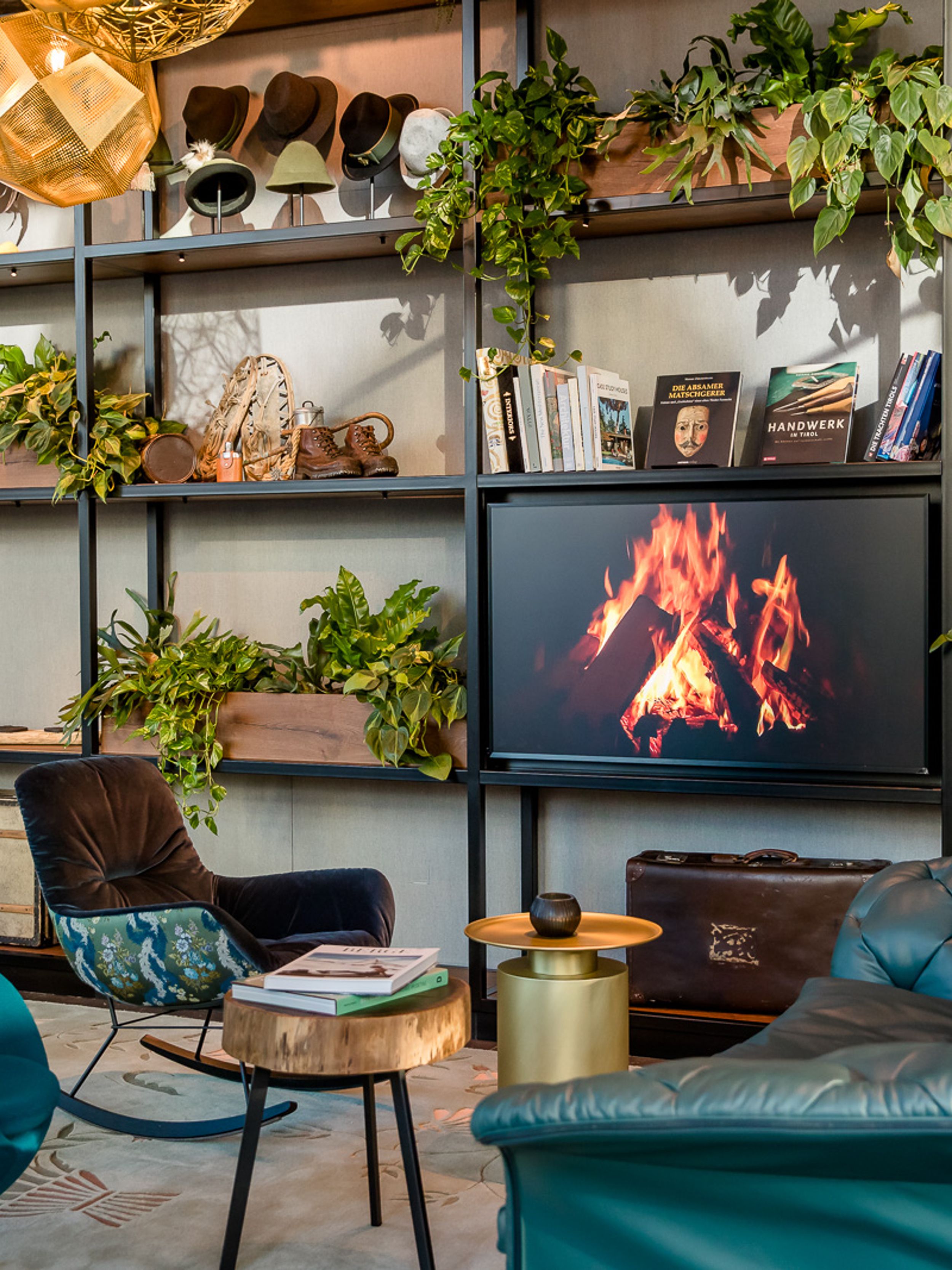 Designhotel Innsbruck Motel One Egg chair und Sofa vor offenem Regal mit Fernseher an der Wand, der ein Lagerfeuer zeigt