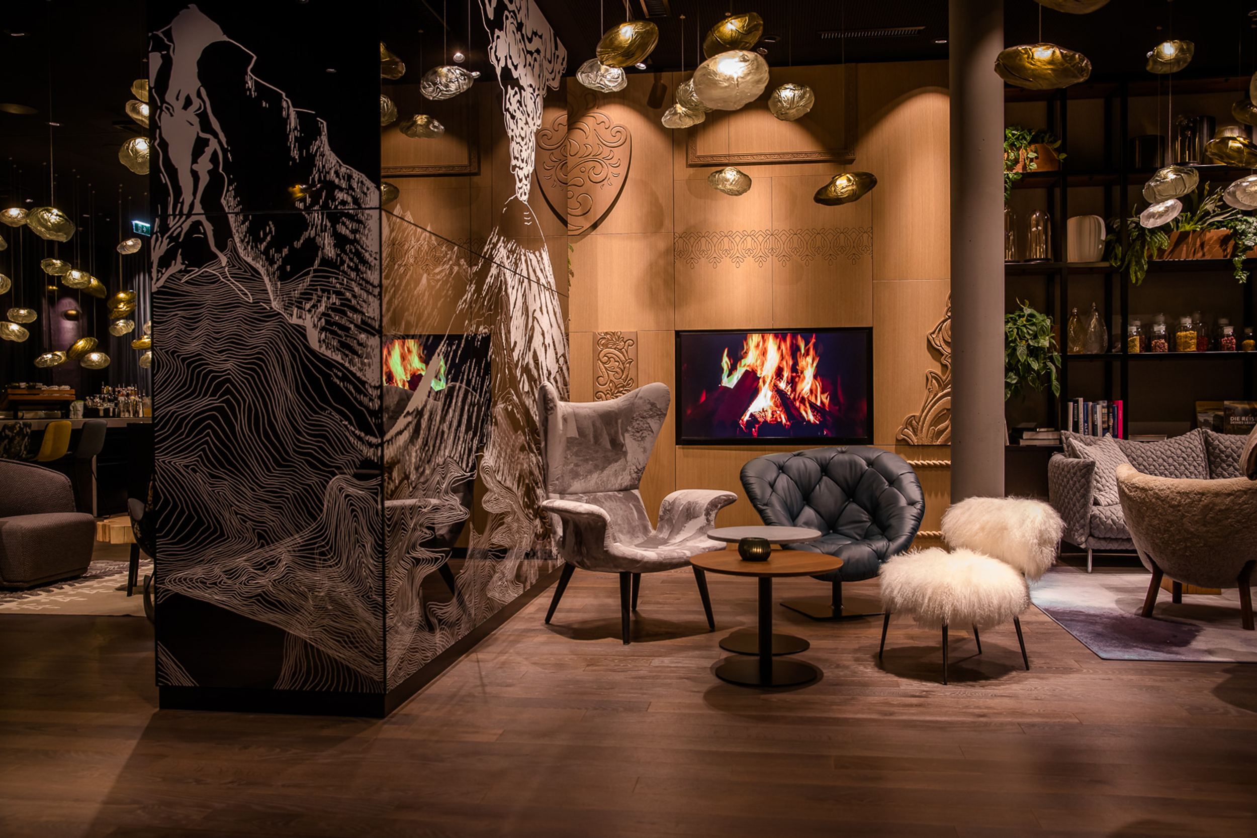 Designhotel Innsbruck Motel One Lounge am Abend mit Sesseln und TV mit Feuer-Motiv an der Wand