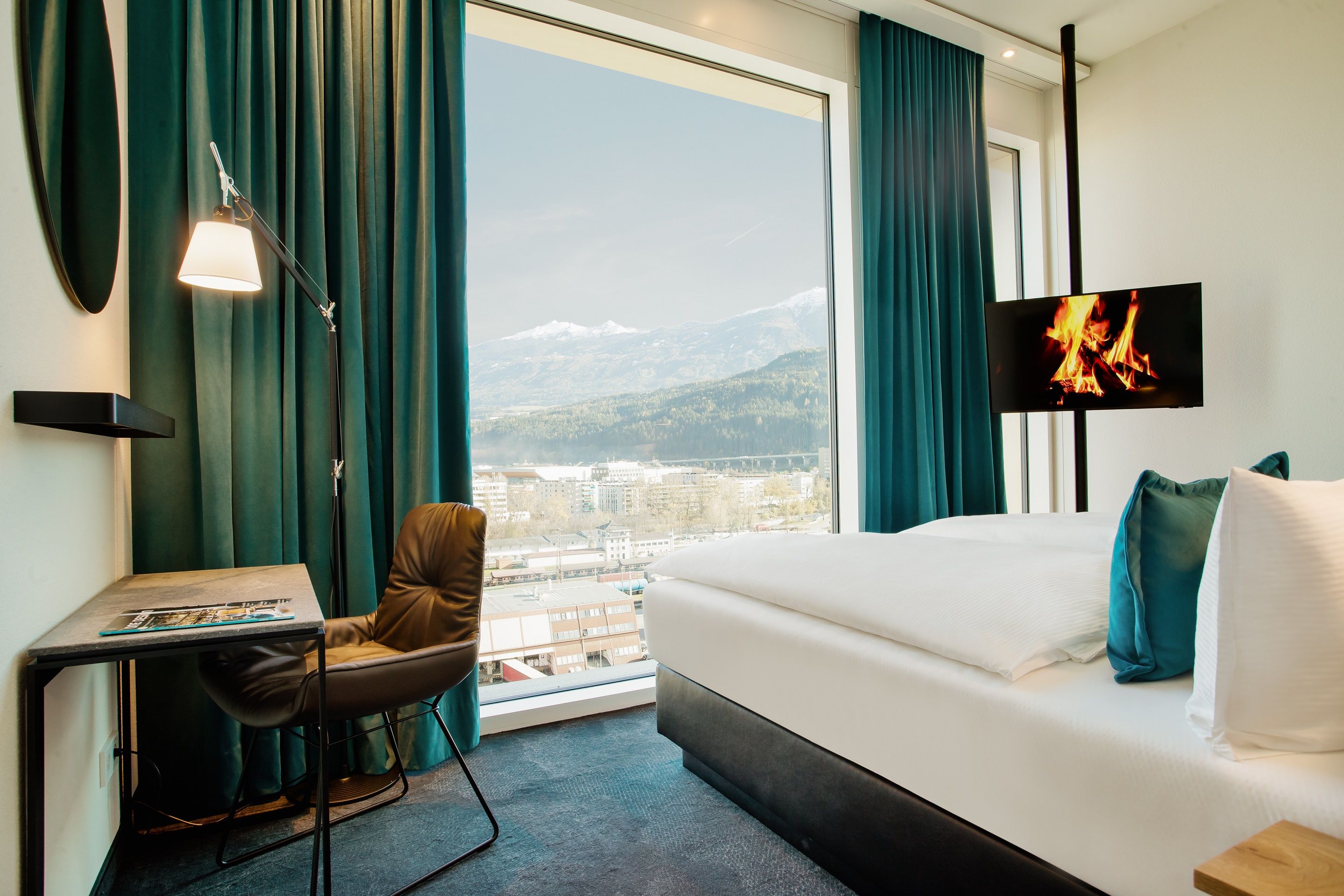 Hotel Innsbruck Motel One helles Zimmer mit Doppelbett, TV, Schreibtisch, Stuhl sowie bodentiefem Fenster