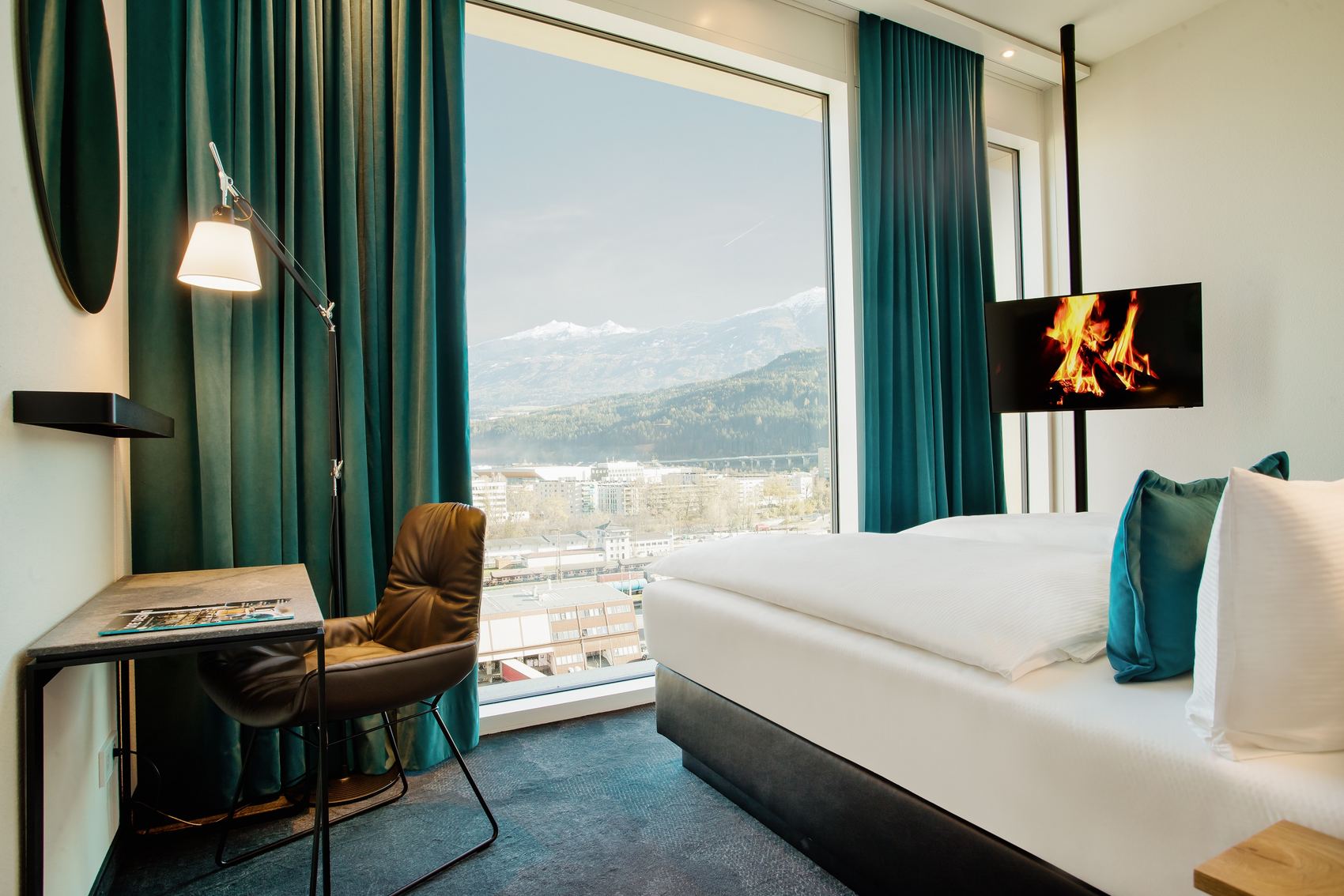 Hotel Innsbruck Motel One helles Zimmer mit Doppelbett, TV, Schreibtisch, Stuhl sowie bodentiefem Fenster