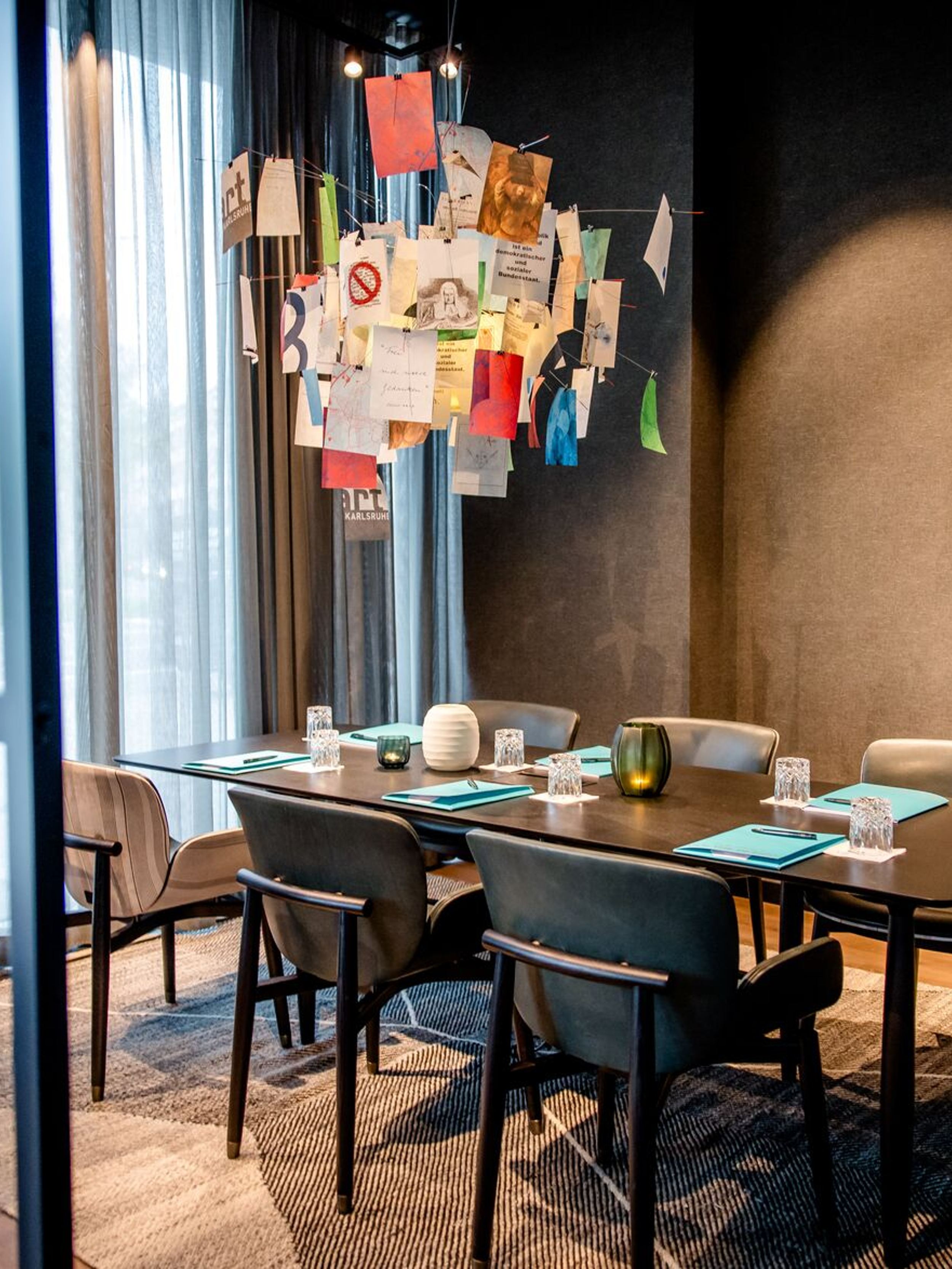 Hotel Karlsruhe Motel One Meetingraum mit Tisch, sechs Stühlen sowie bodentiefem Fenster für viel Licht