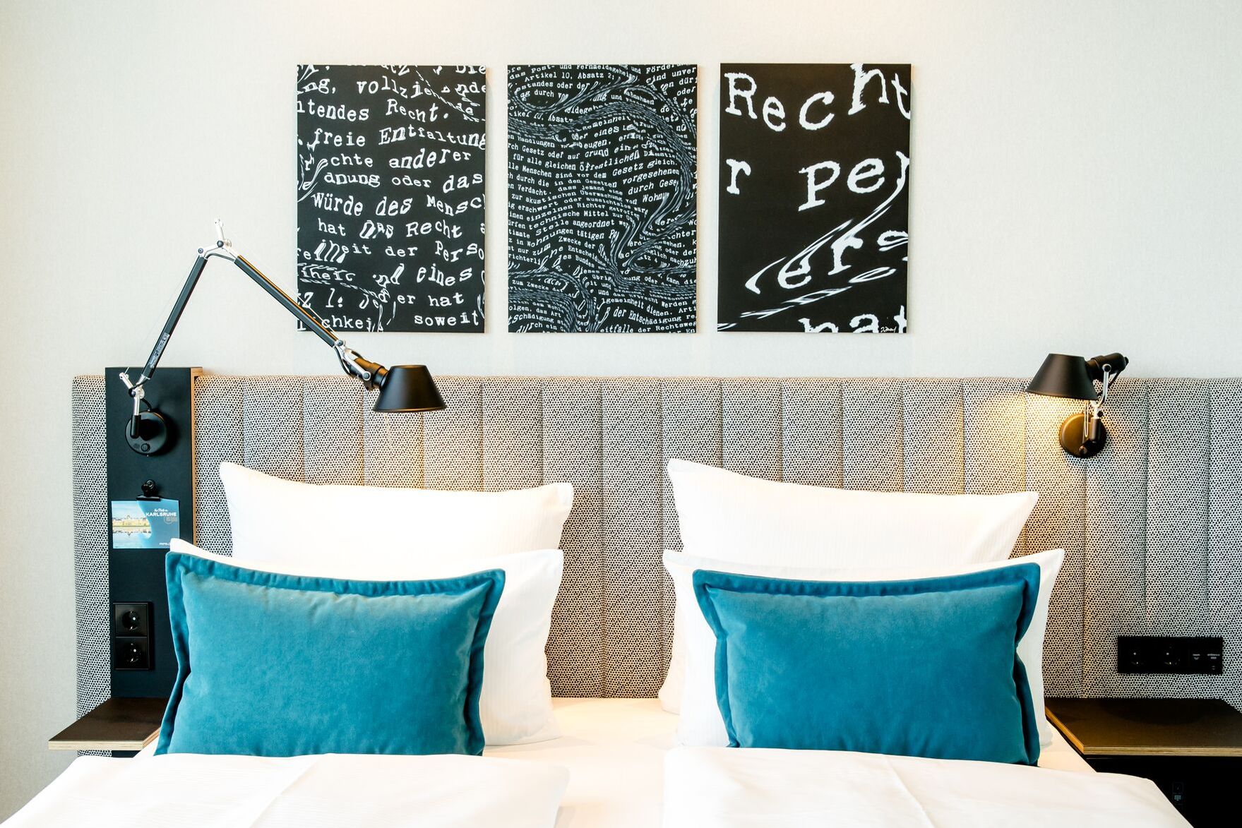 Hotel Karlsruhe Motel One helles Hotelzimmer mit Blick auf Bett mit Zierkissen in türkis