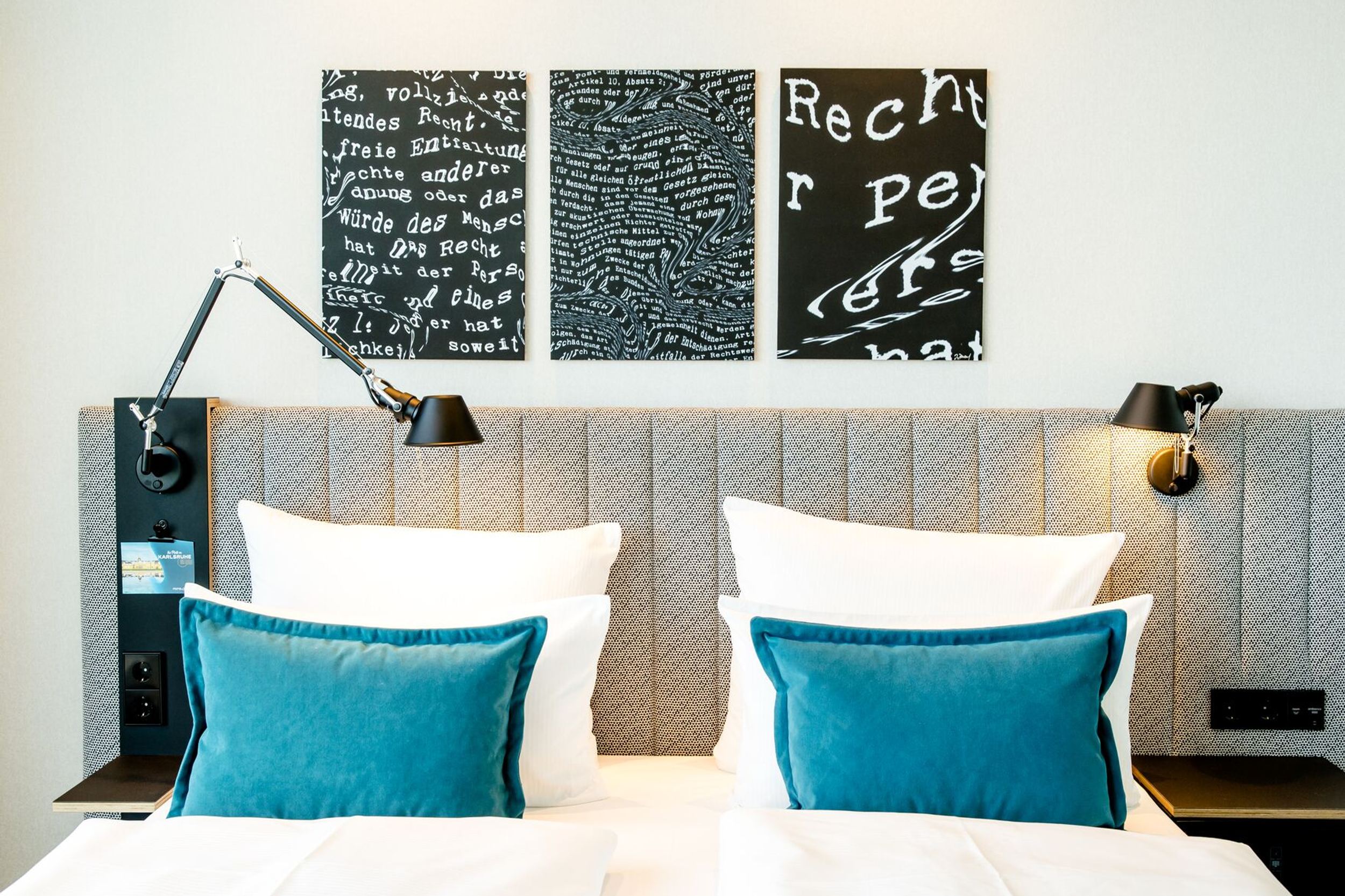 Hotel Karlsruhe Motel One helles Hotelzimmer mit Blick auf Bett mit Zierkissen in türkis