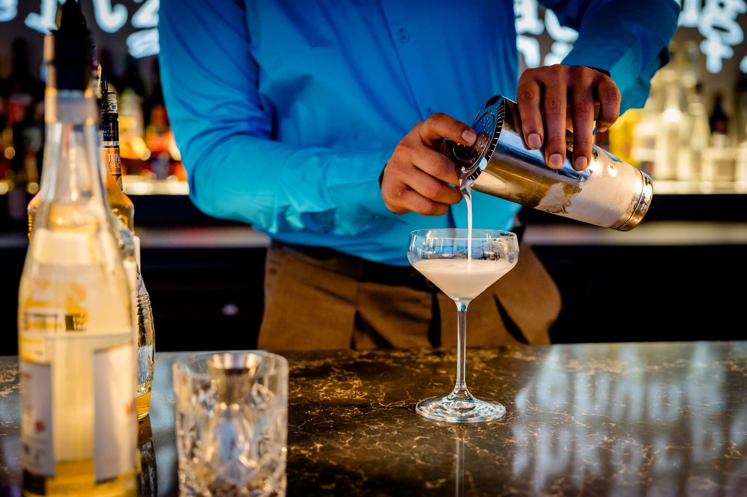 Designhotel Karlsruhe Motel One Rooftop Bar Barkeeper gießt einen cremigen Cocktail aus einem Shaker in ein elegantes Cocktailglas an der Bar.