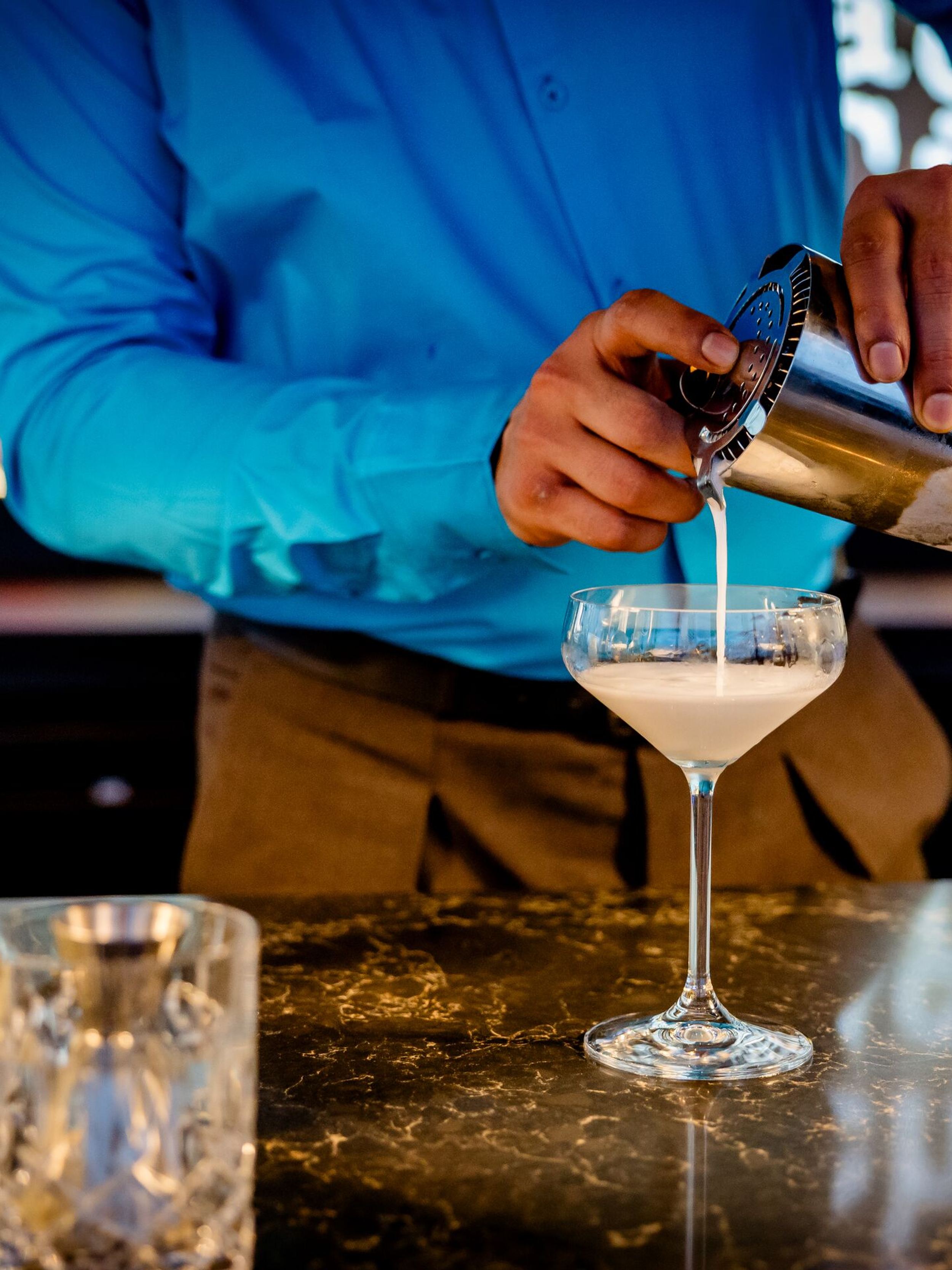 Designhotel Karlsruhe Motel One Rooftop Bar Barkeeper gießt einen cremigen Cocktail aus einem Shaker in ein elegantes Cocktailglas an der Bar.
