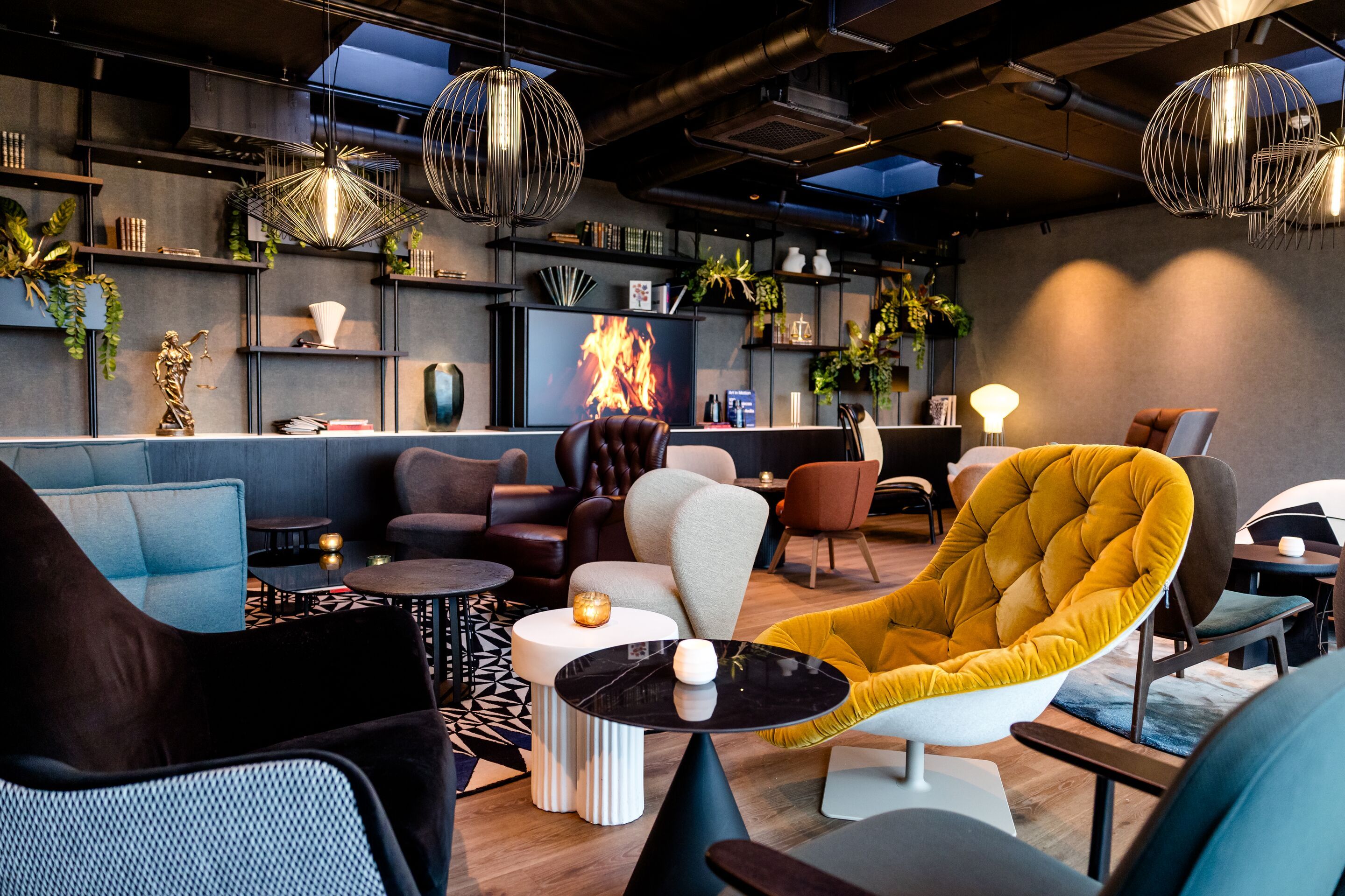 Hotel Karlsruhe Motel One Rooftop Bar großer Sitzbereich mit gemütlichen Sesseln, Kaminfeuer auf TV und stilvoller Beleuchtung.