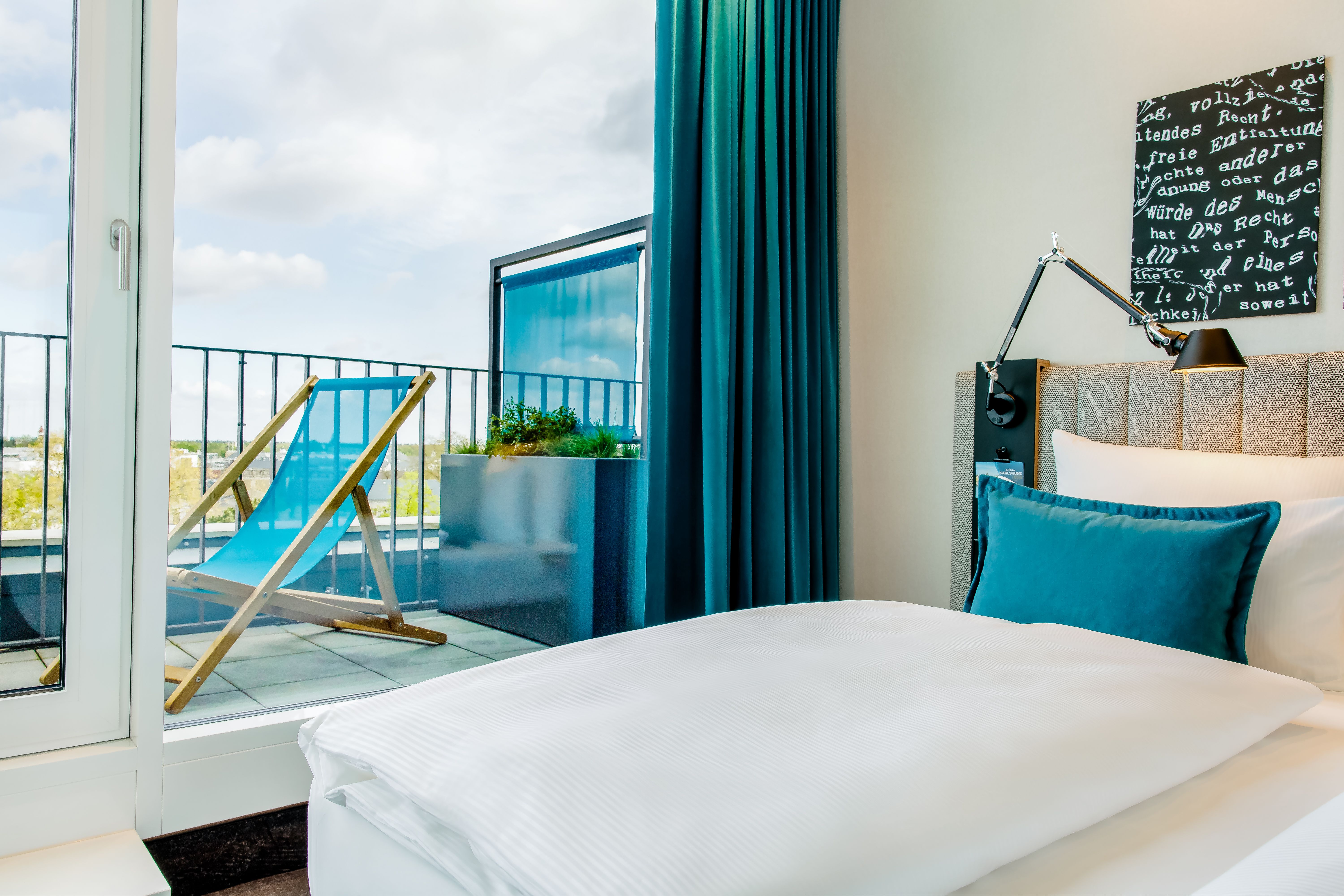 Designhotel Karlsruhe Motel One Balkonzimmer mit Blick über das Bett auf einen Liegestuhl auf dem Balkon