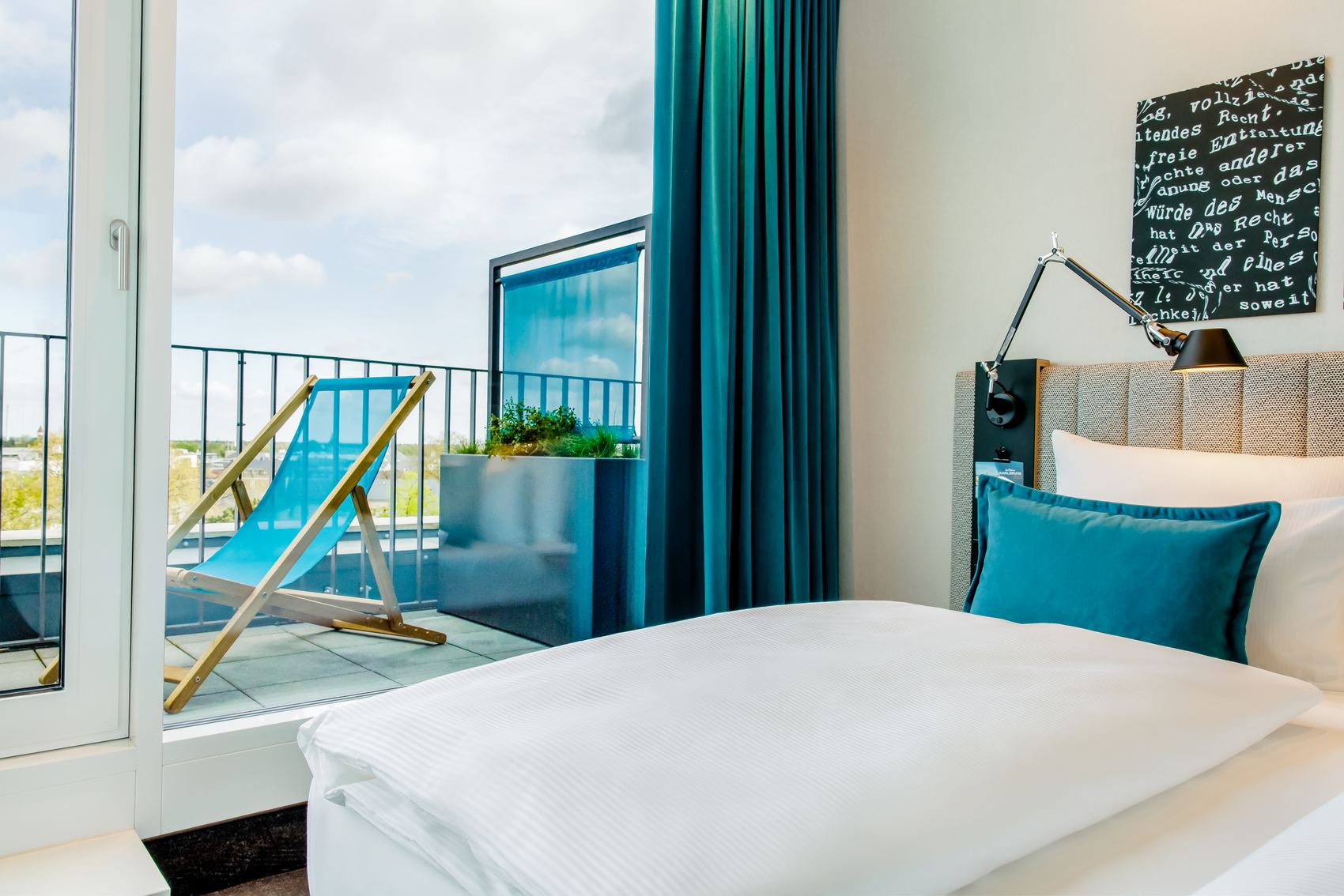 Designhotel Karlsruhe Motel One Balkonzimmer mit Blick über das Bett auf einen Liegestuhl auf dem Balkon